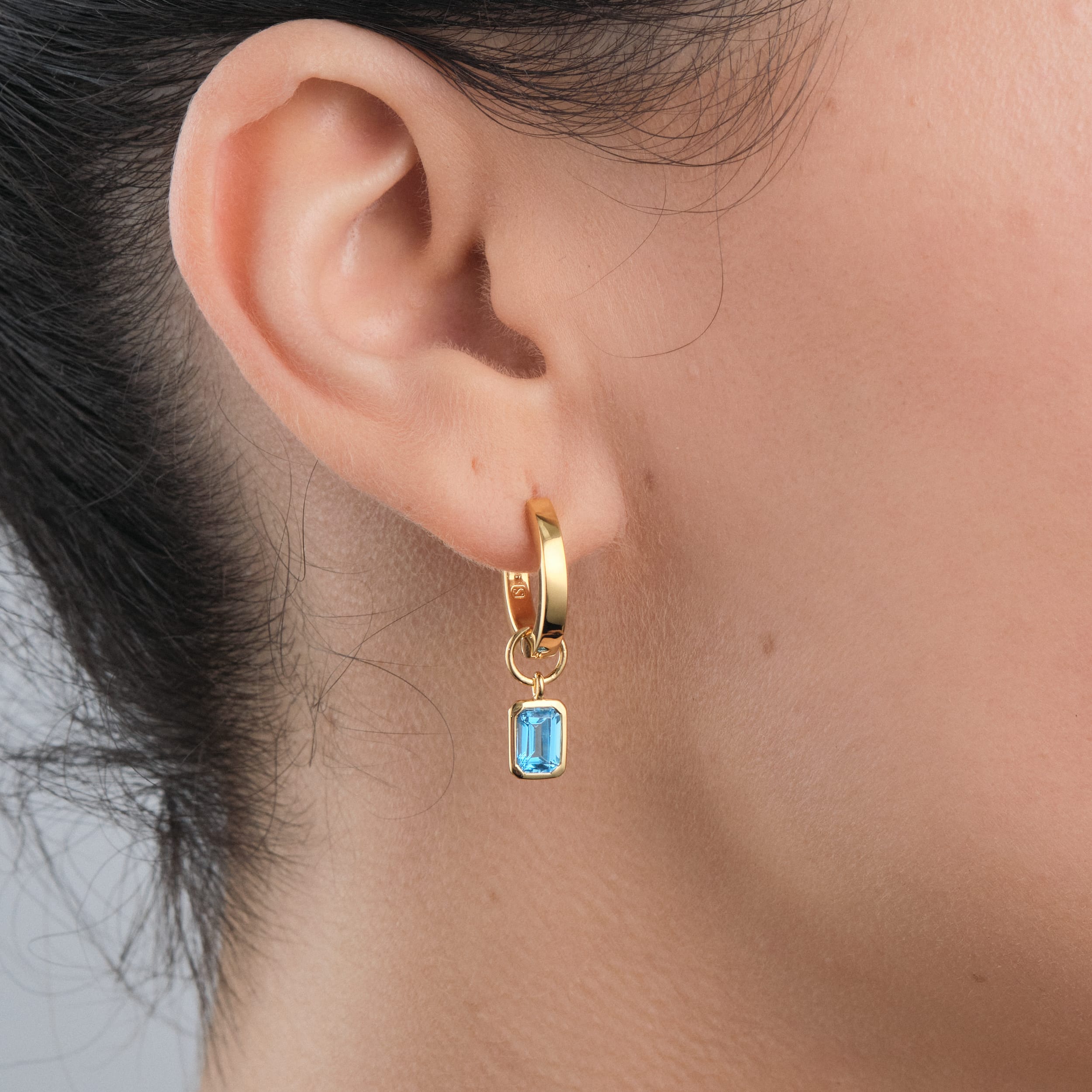 Side view of 18k luxurious Gold Vermeil Huggie hoop earrings with interchangeable blue topaz gemstone charms.