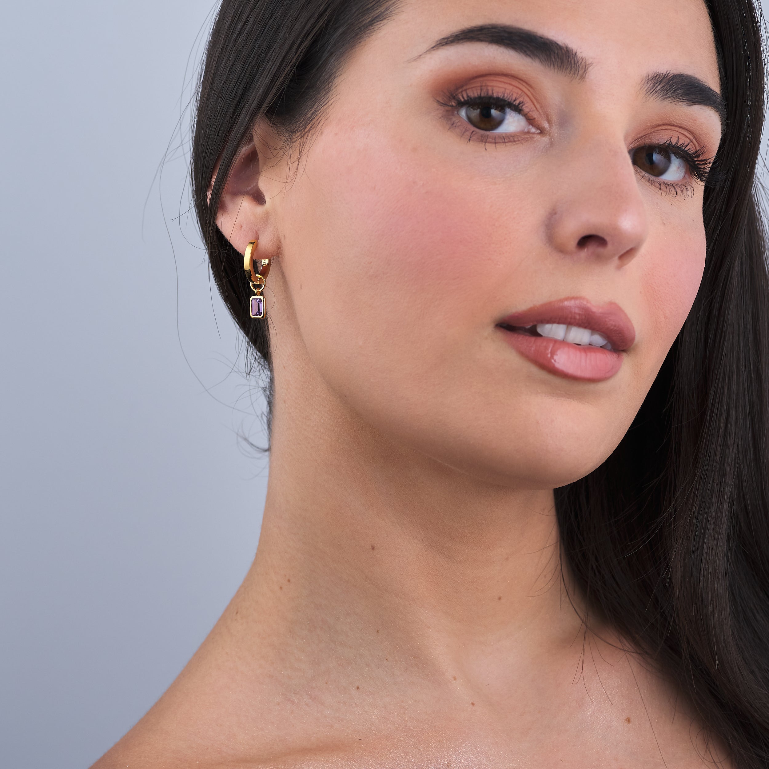 Woman wearing 18K gold vermeil amethyst huggie hoop earrings showcasing amethyst, February's birthstone, with interchangeable charms. Made from high-quality 18K gold vermeil, offering an affordable yet luxurious gift option with lasting elegance.