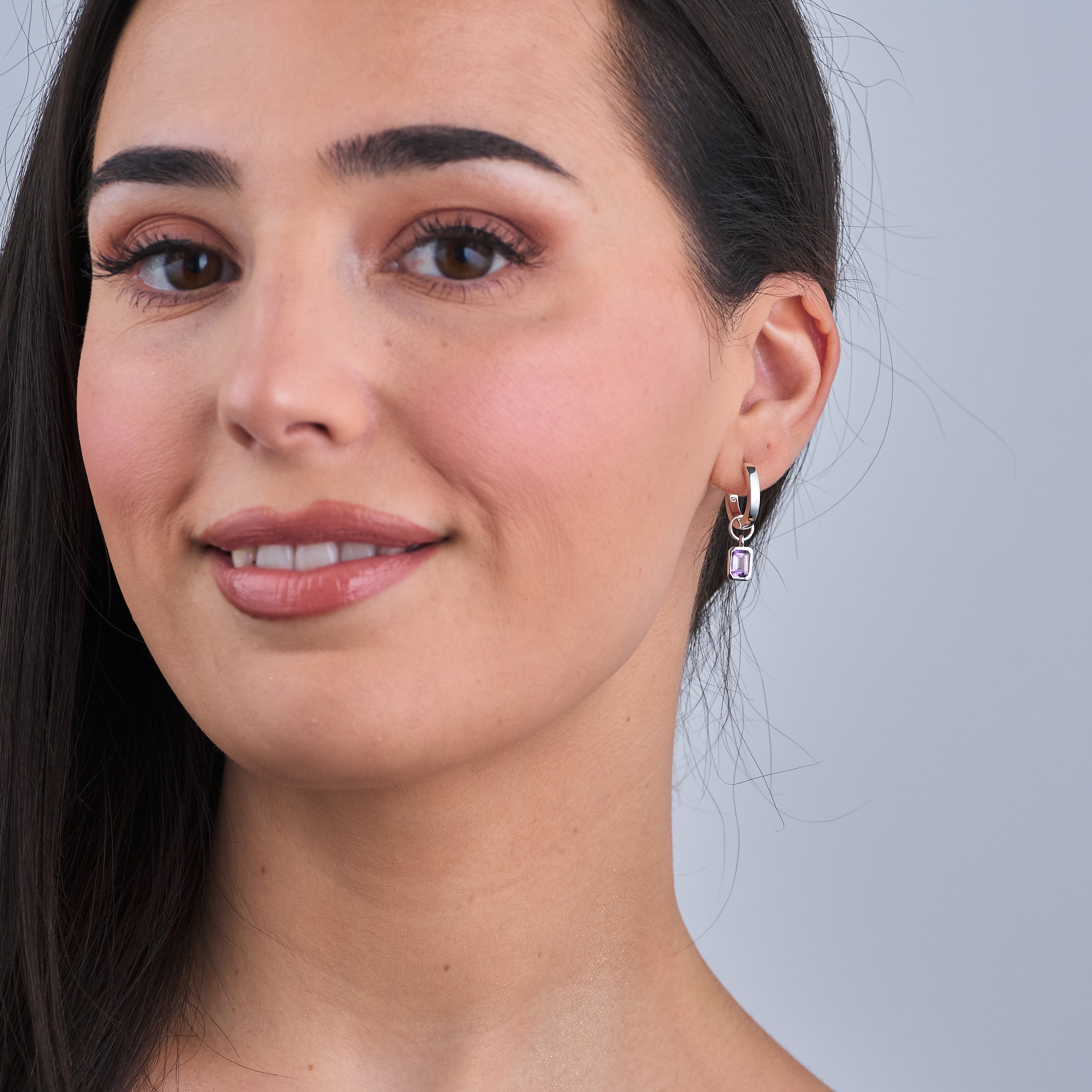 Woman wearing Sterling silver amethyst huggie hoop earrings featuring amethyst, the February birthstone, with interchangeable charms. Crafted from high-quality, hypoallergenic sterling silver for durability and elegance, making them the perfect personalised gift.