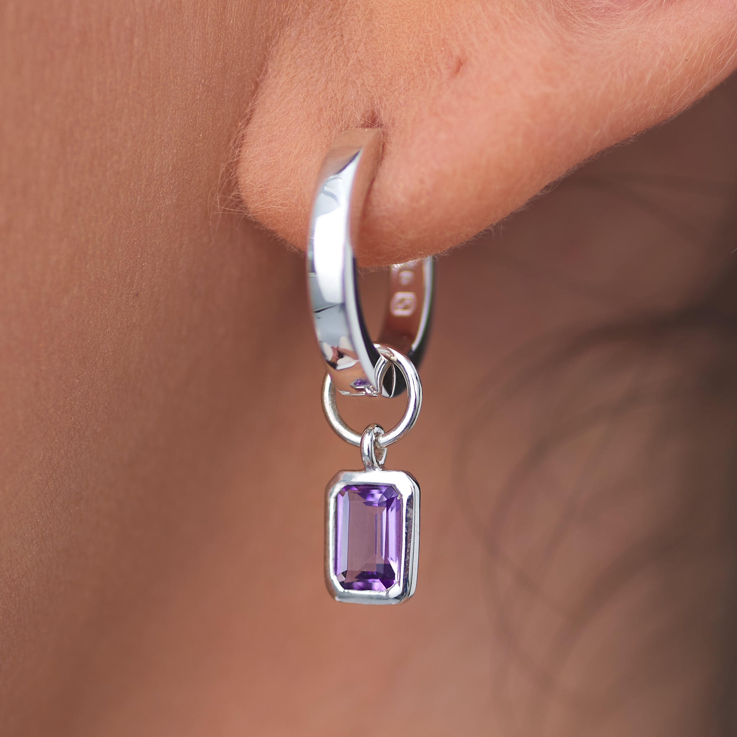 Close-up of sterling silver amethyst Huggies hoop earrings with interchangeable charms and amethyst, February's birthstone. Crafted from premium, hypoallergenic sterling silver for a perfect gift with timeless elegance
