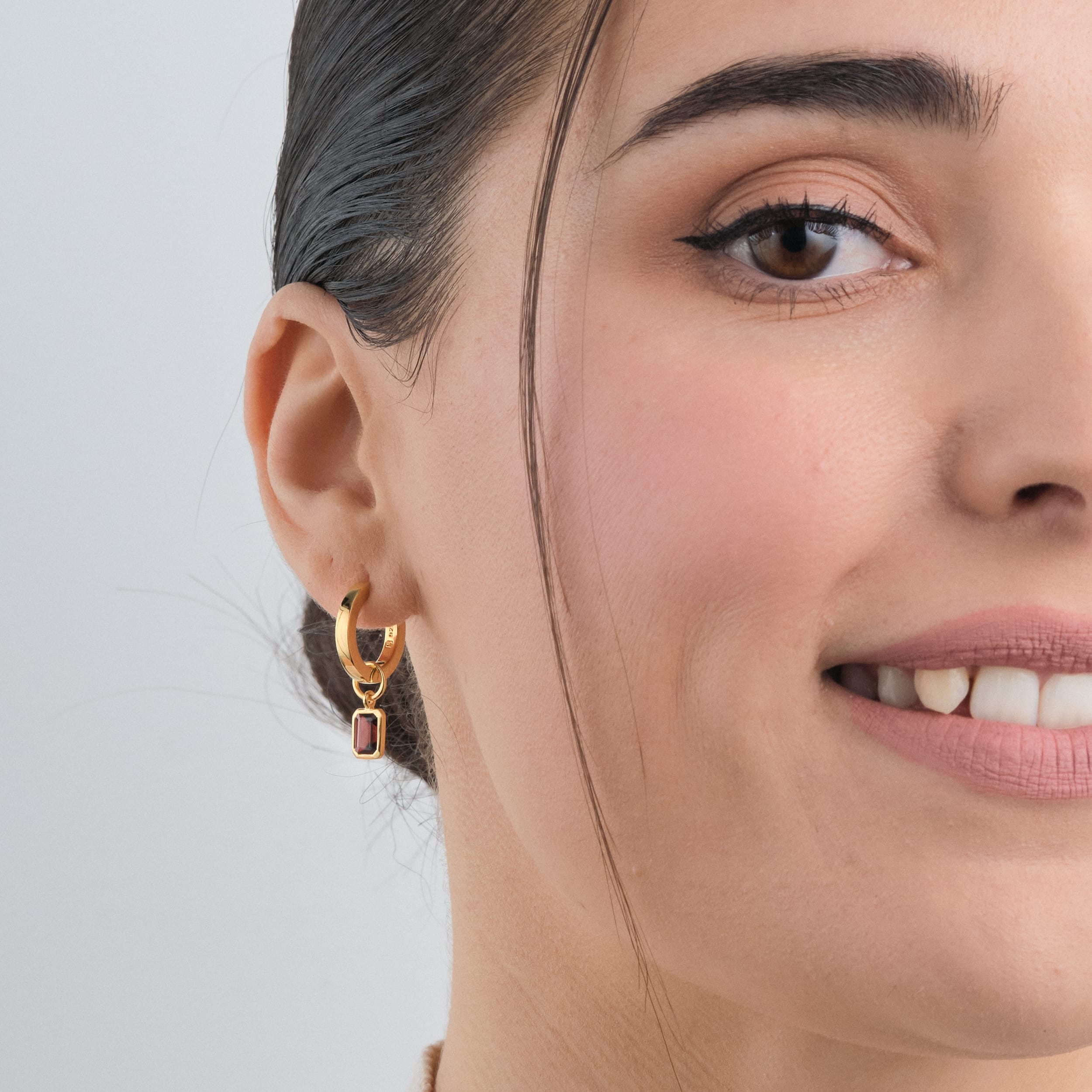 Red Garnet January birthstone Gemstone Charms in 18k Gold Vermeil attached to the perfect pair of huggie hoops being worn by a woman front view.