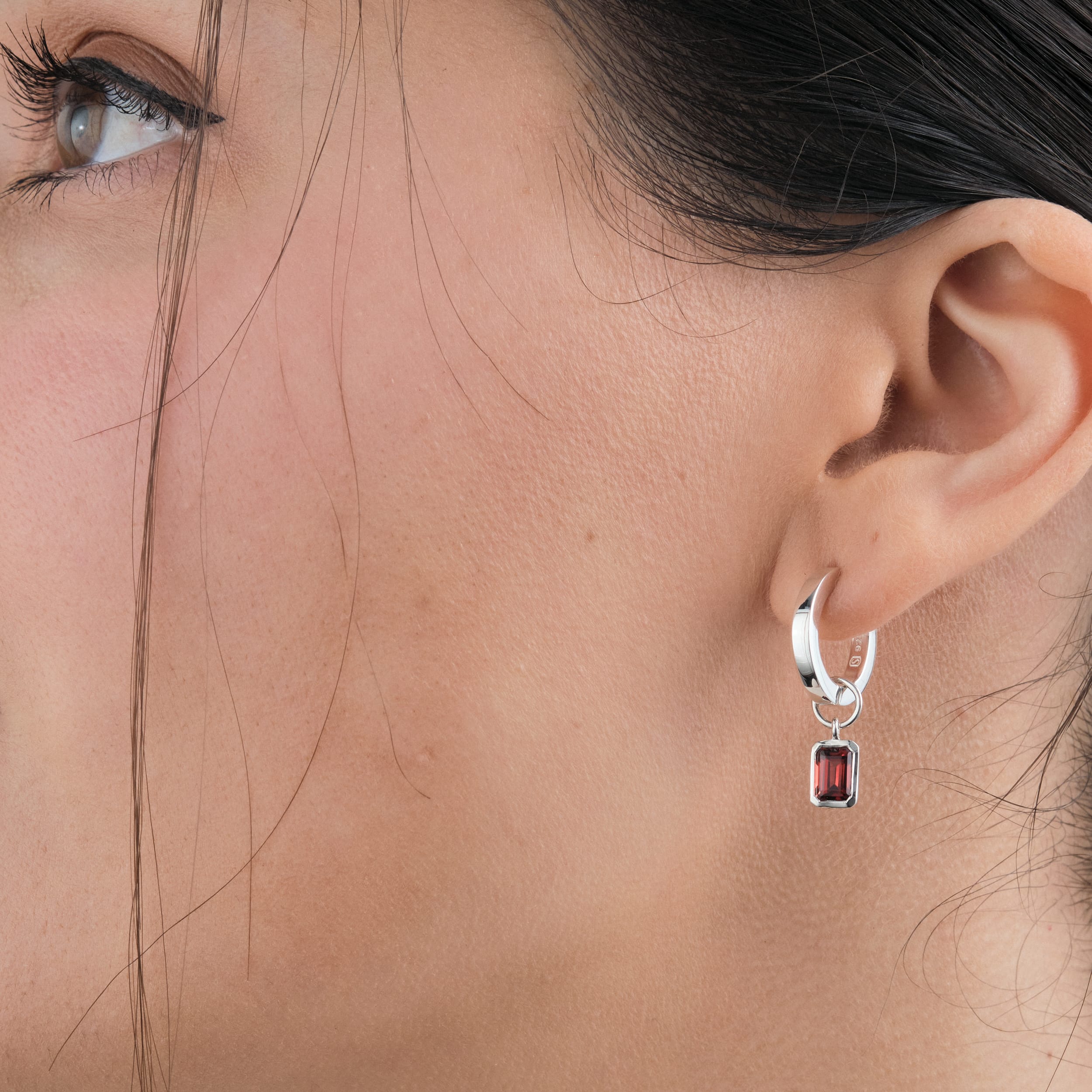 Side view of a woman wearing premium sterling silver hugger hoop earrings that are tarnish and nickel free with detachable red garnet gemstone charms. The perfect gift for those born in January and those who love personalised jewellery.