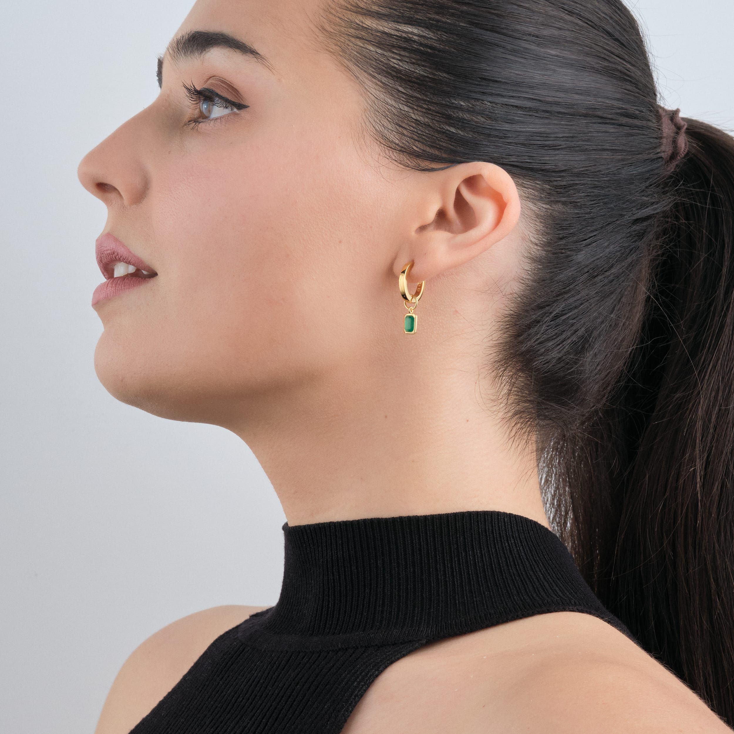Side view of a woman wearing 18K gold vermeil huggie hoop earrings with interchangeable green onyx gemstone charms. A perfect, customisable gift featuring May’s birthstone, crafted in high-quality, budget-friendly gold vermeil for long-lasting elegance.