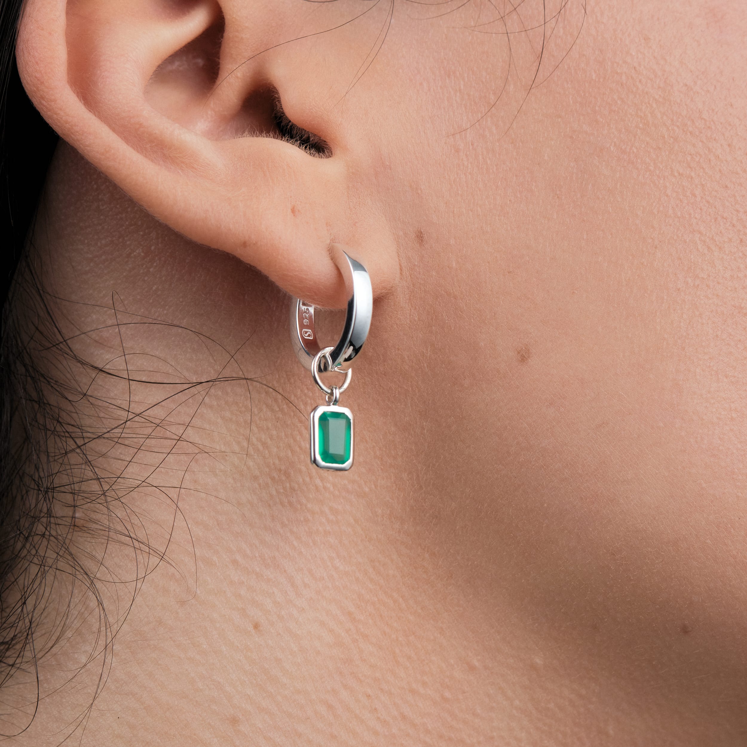 A woman wearing sterling silver huggie hoop earrings with interchangeable green onyx gemstone charms designed with hypoallergenic sterling silver, these earrings showcase May's birthstone, green onyx, making them a meaningful and stylish gift.