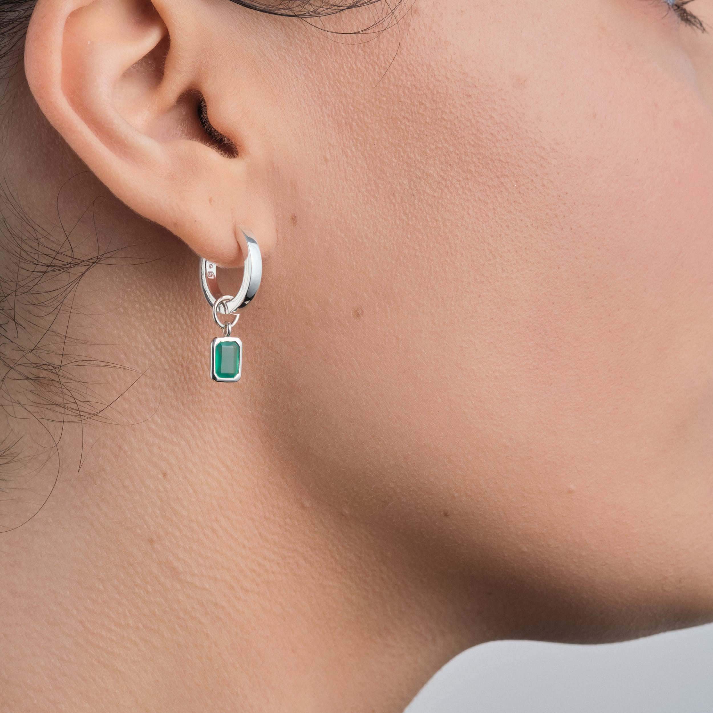 Side view of a woman wearing 18K gold vermeil huggie hoop earrings with interchangeable green onyx gemstone charms. Designed for everyday wear with the lasting quality of gold vermeil, these May birthstone earrings are a stylish and affordable jewellery choice.