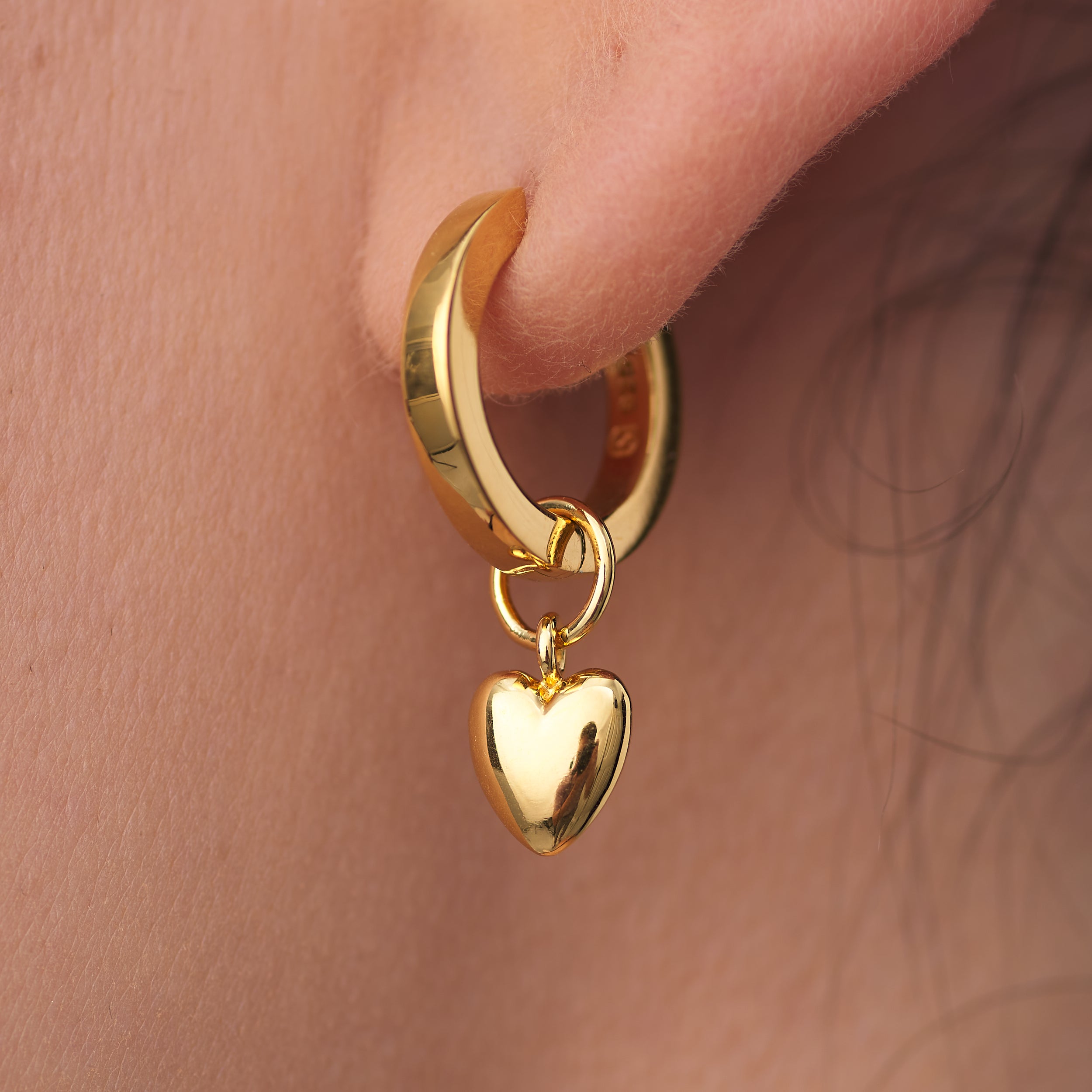 Close-up of puffy heart charm huggie hoop earrings in 18K gold vermeil, interchangeable charms allow for endless customisation, offering a perfect, personalised gift option.