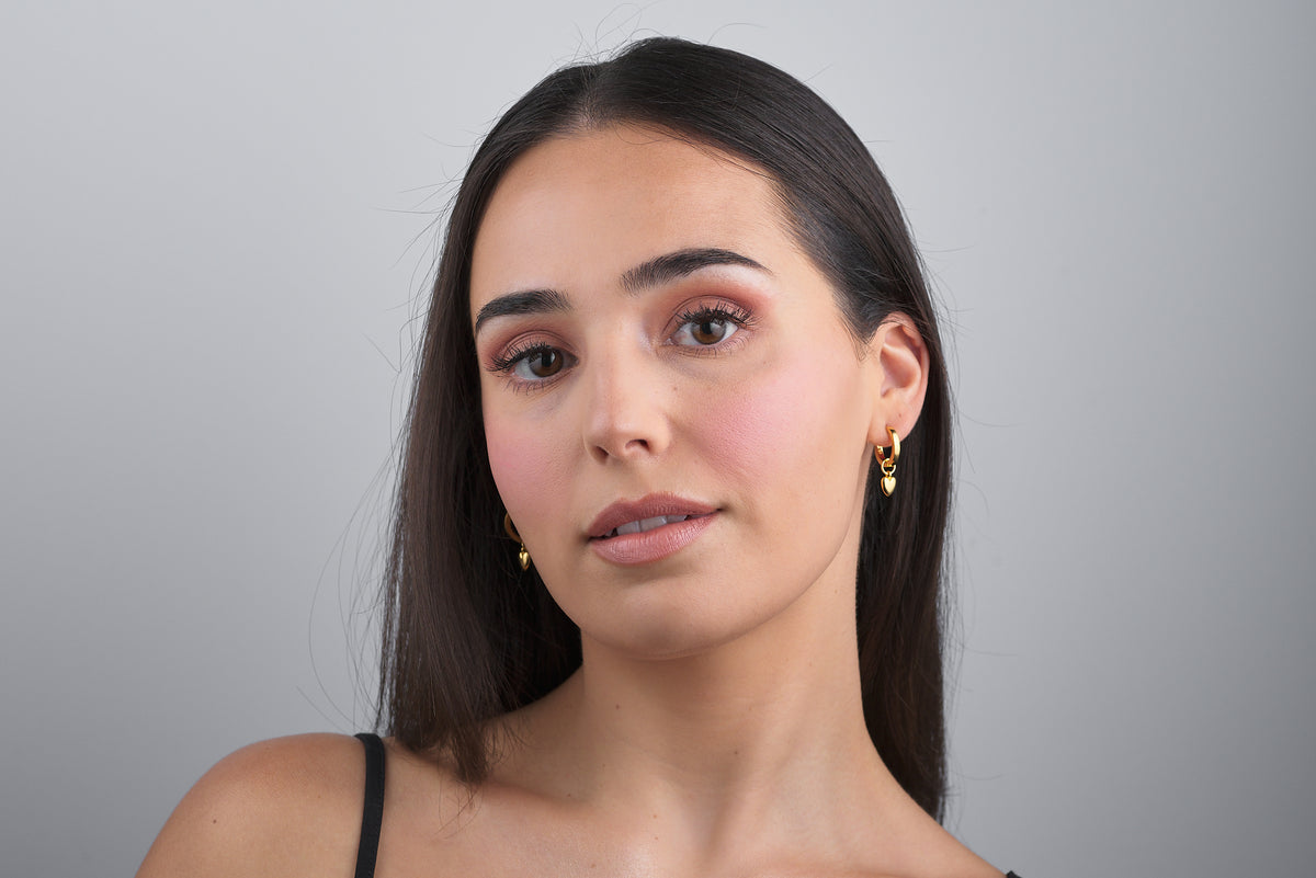 woman wearing 18k gold vermeil huggie hoop earrings with heart charms attached