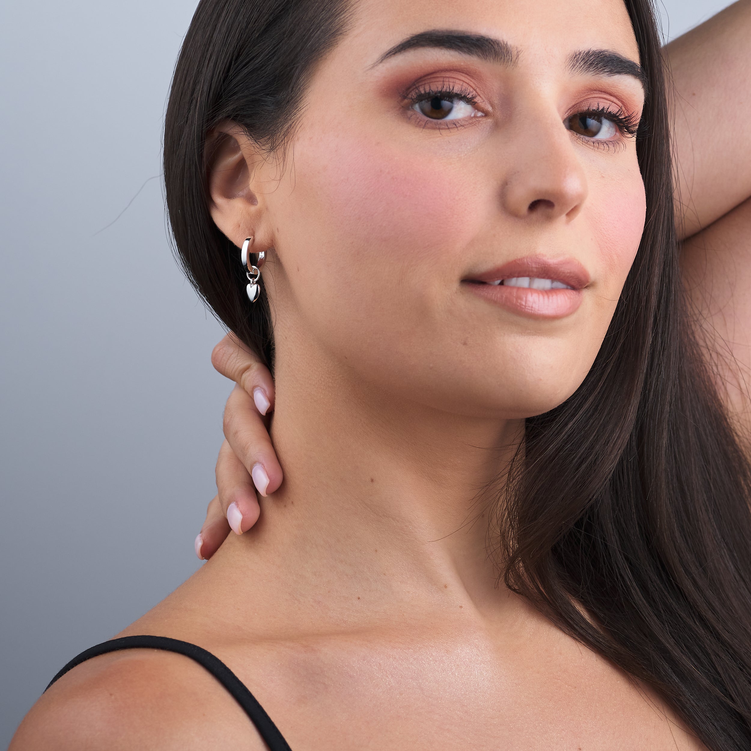 A woman wearing puffy heart charm huggie hoop earrings in sterling silver, elegant and chic, crafted from durable, hypoallergenic sterling silver for everyday wear and lasting shine.