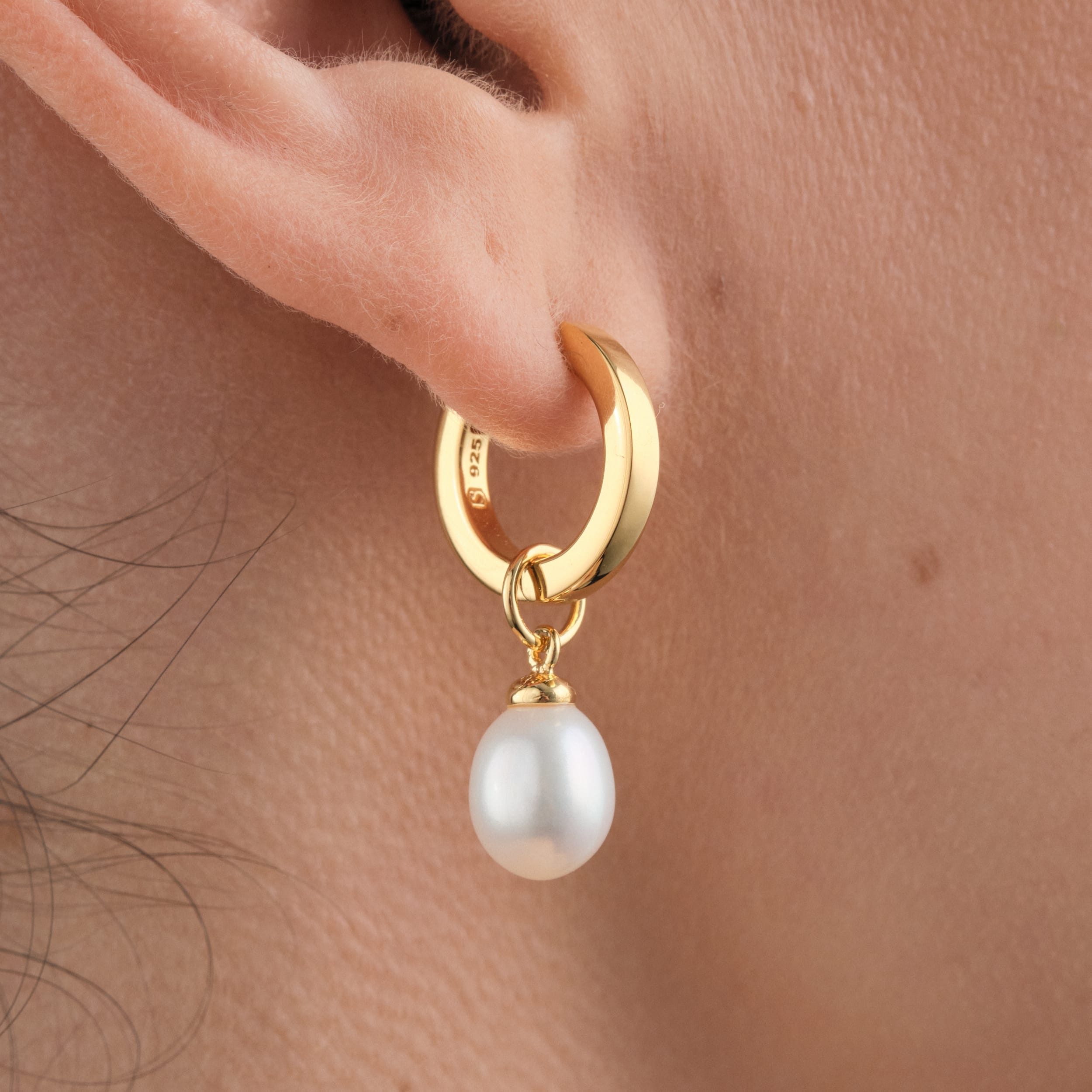 Close up of elegant 18K gold vermeil huggie hoop earrings with interchangeable pearl charms designed for versatility, allowing customisation for any occasion, including weddings. Offering lasting durability and an affordable luxury option for a timeless gift or accessory.