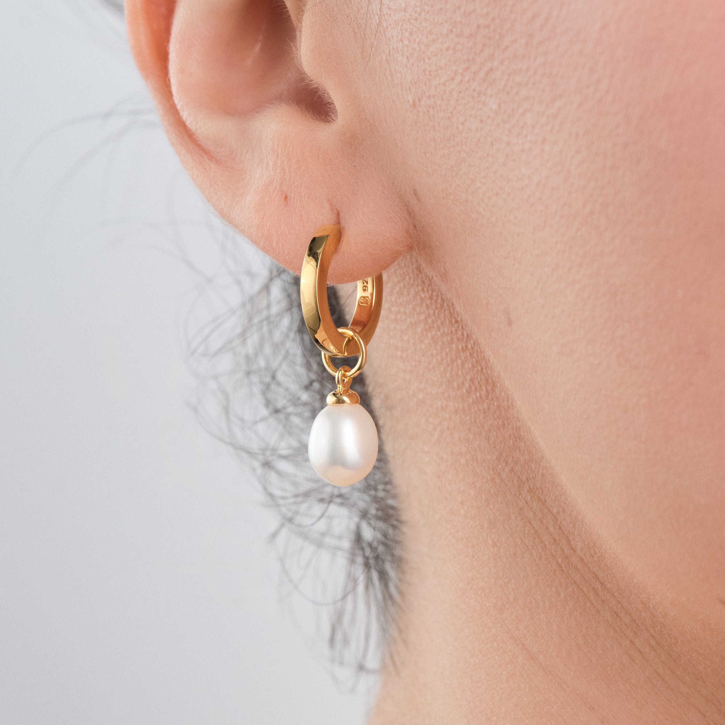 Close up front view of a woman wearing 18K gold vermeil huggie hoop earrings with interchangeable pearl charms customisable and versatile, ideal for weddings or as a unique gift. Built for durability with 18K gold vermeil, they provide a high-quality, affordable luxury option for every occasion.
