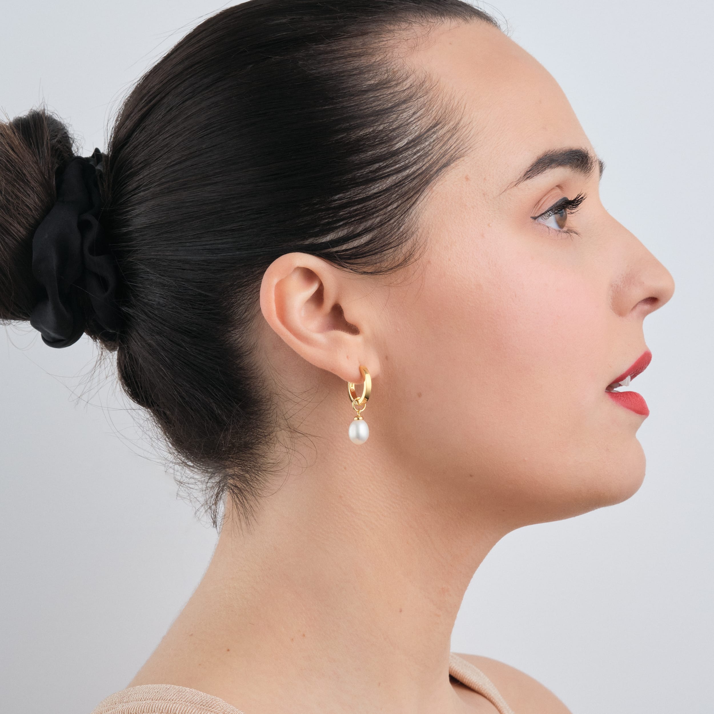 Side view of a woman wearing 18K gold vermeil huggie hoop earrings with interchangeable pearl charms. Perfect for customising to any style, these earrings make a stunning wedding accessory or gift. Made with durable 18K gold vermeil for lasting beauty at an affordable price.