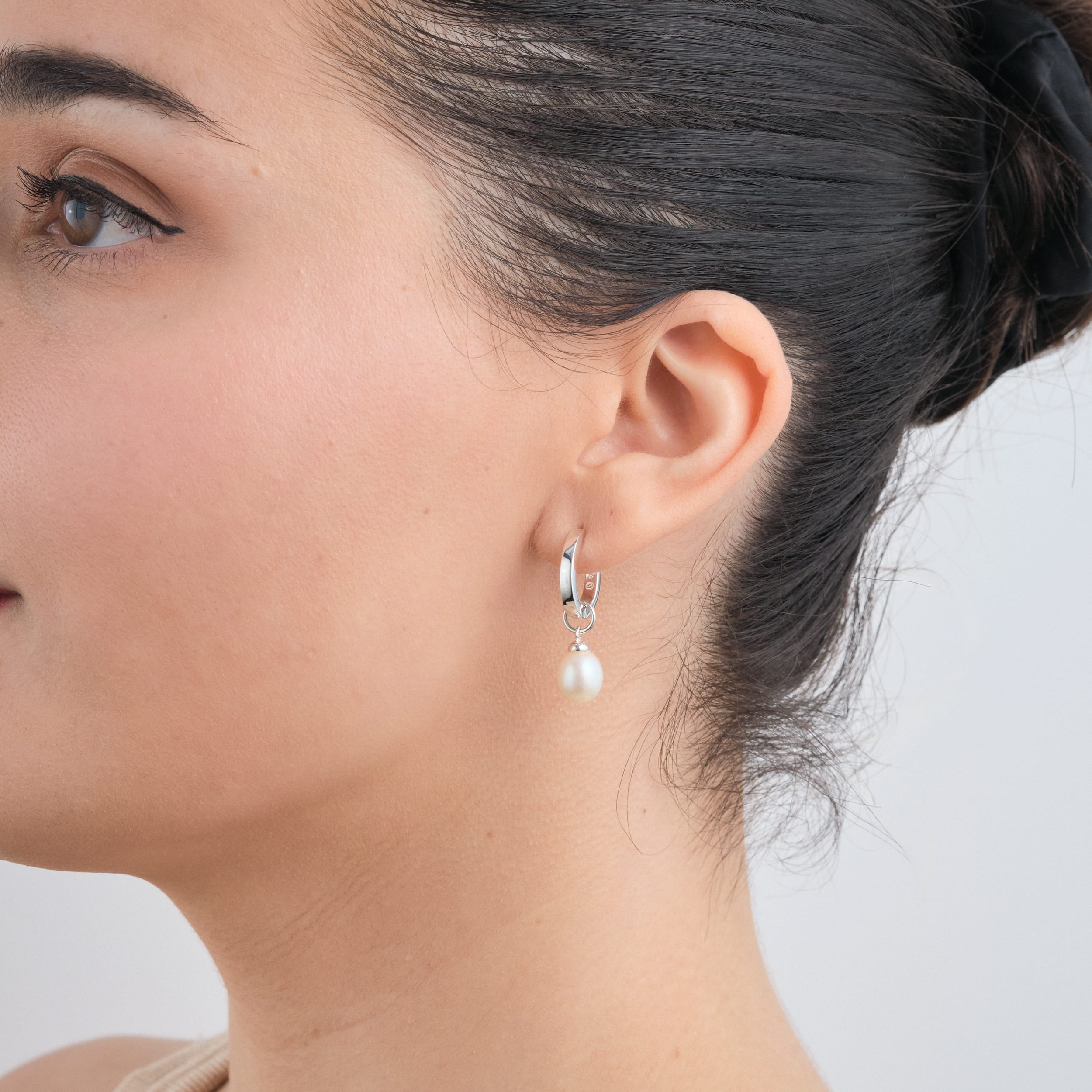 Close-up of sterling silver huggie hoop earrings with pearl charms. Made from hypoallergenic sterling silver, these charms can be customised, providing a perfect, comfortable touch for wedding jewellery.
