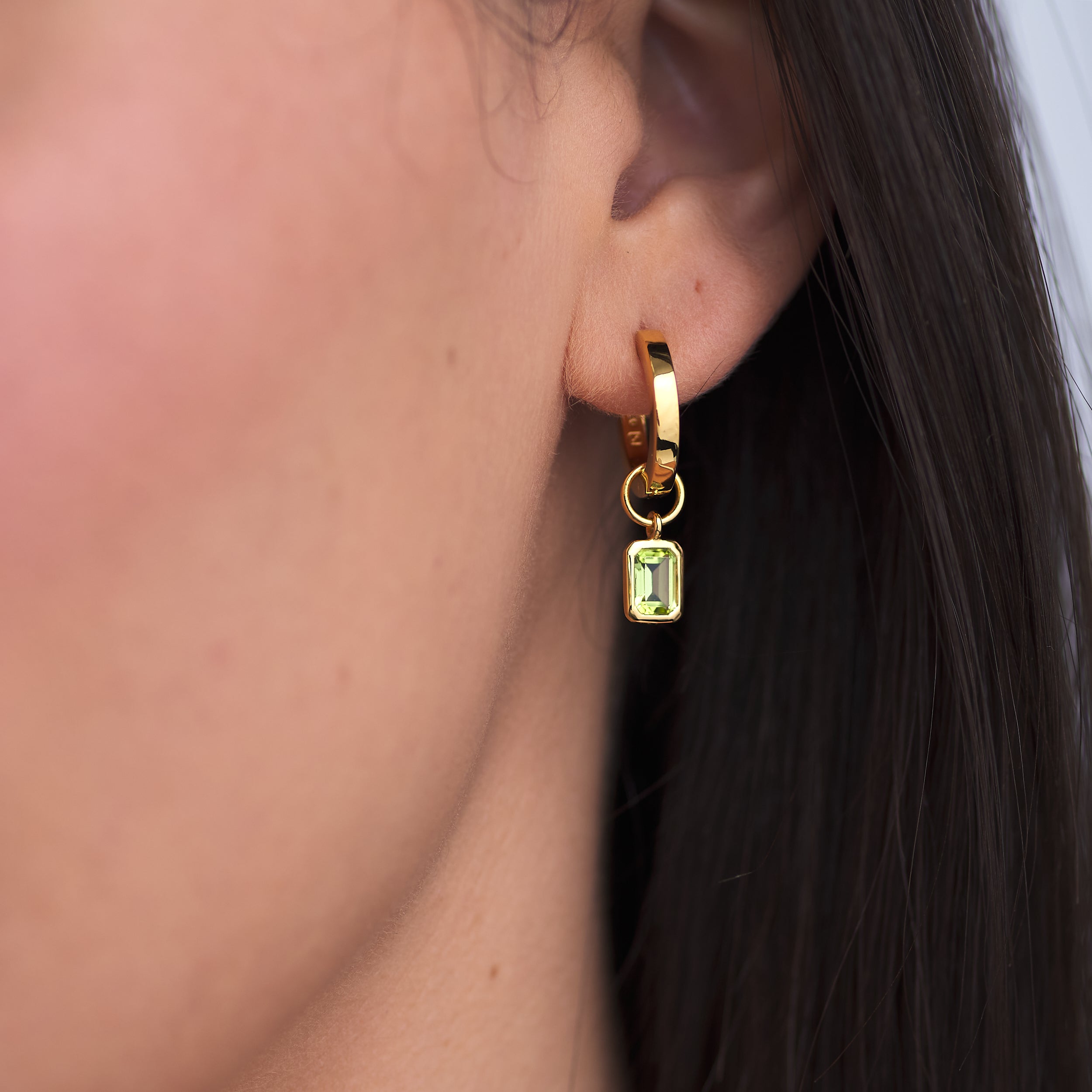 Luxury Huggie hoop earrings in 18k Gold Vermeil with detachable birthstone Peridot charm attached to a woman's ear.