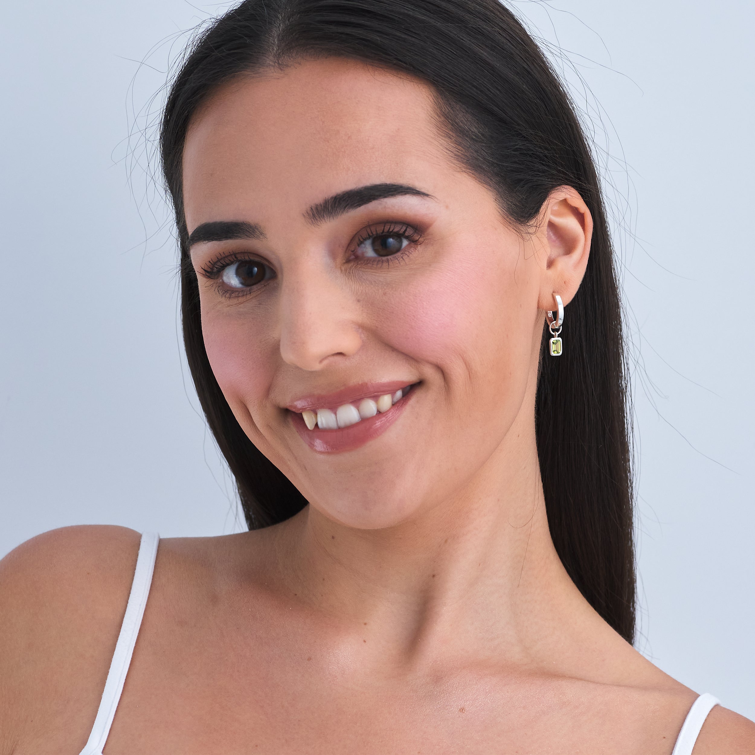 Woman wearing Peridot gemstone charm earring in Sterling Silver attached to a classic Huggie Hoop earring.