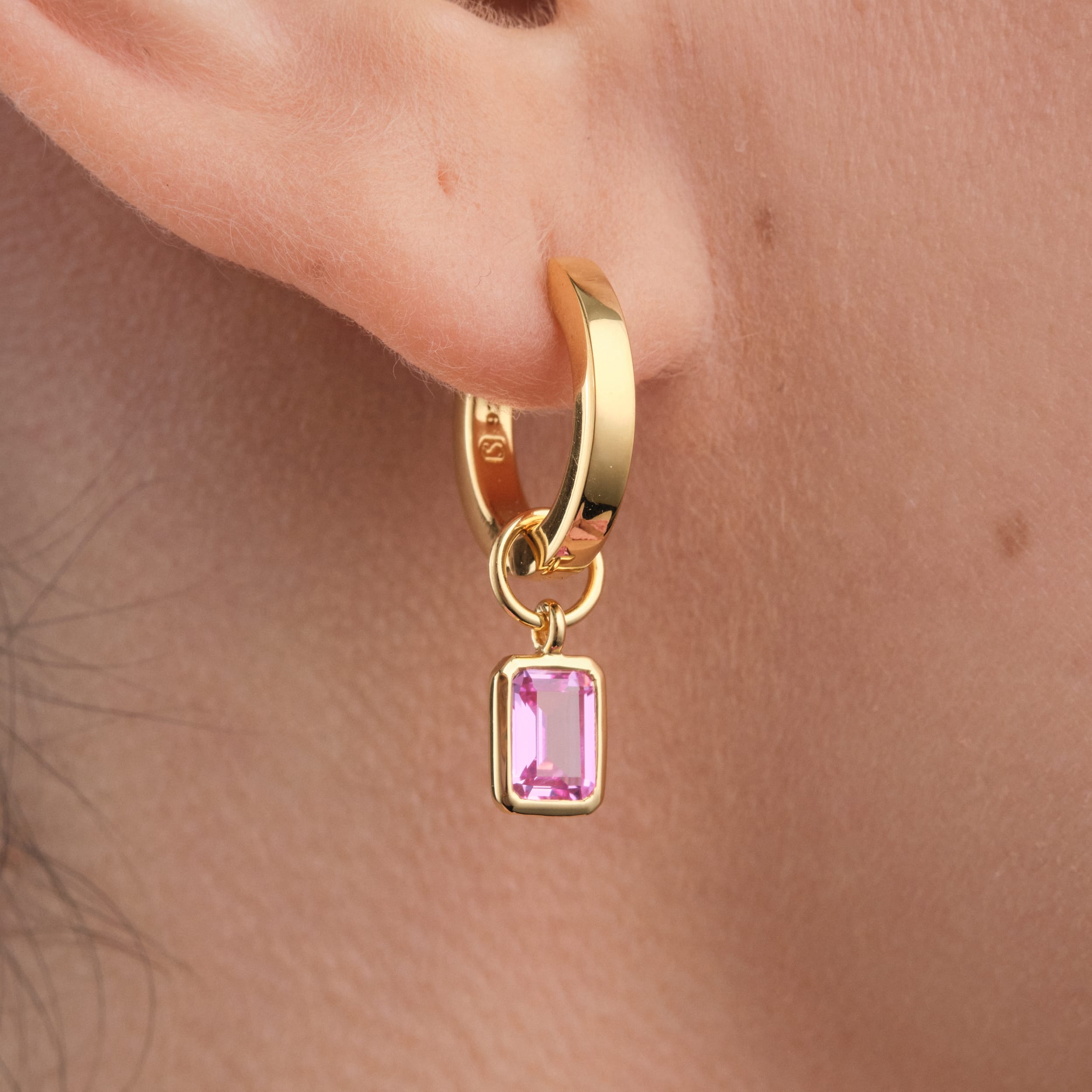 Close-up of 18K gold vermeil huggie hoop earrings with detachable pink ruby gemstone charms designed for versatility, these affordable and durable earrings allow for effortless styling, making them a perfect gift or everyday essential.