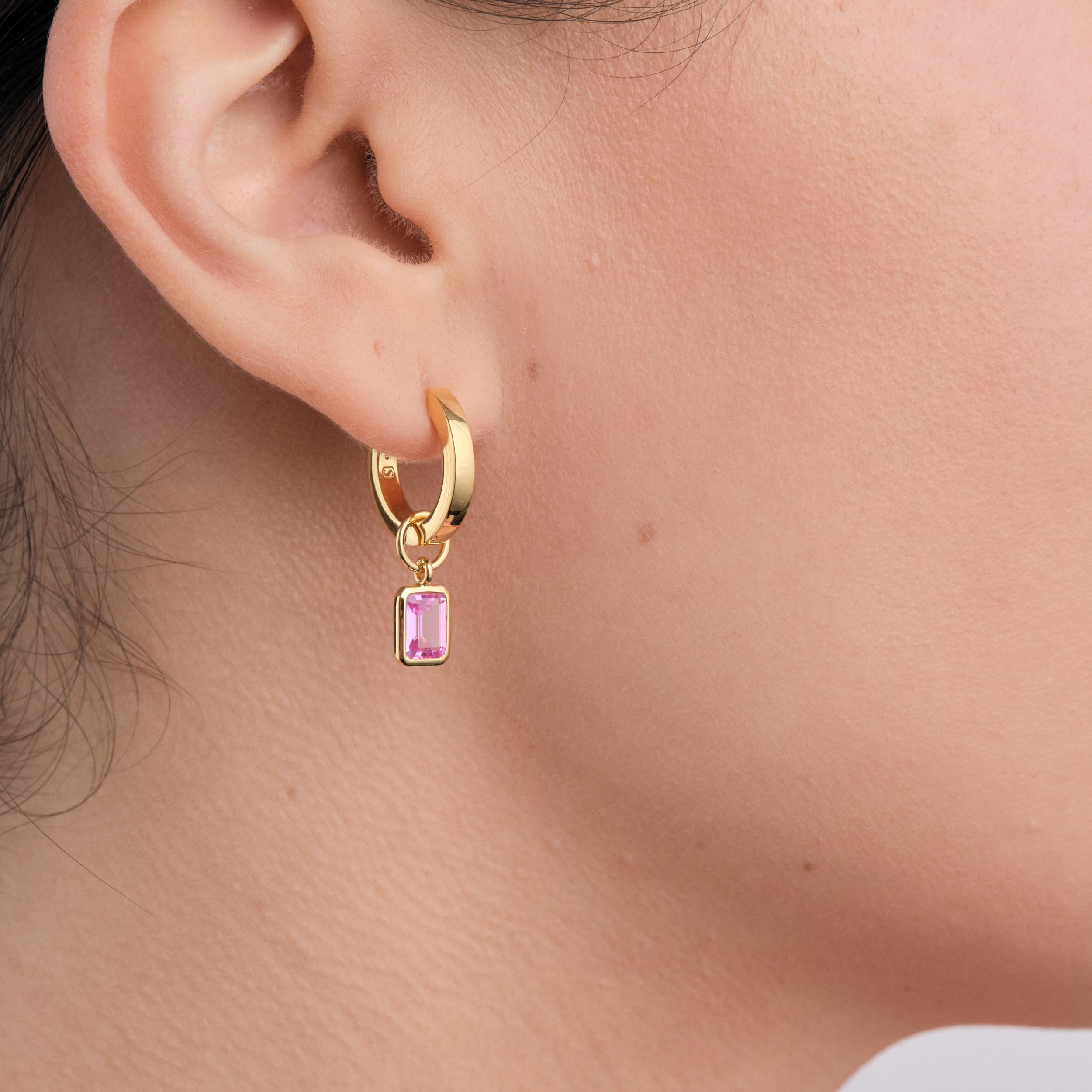 Close up image of a woman wearing 18K gold vermeil huggie hoop earrings with interchangeable pink ruby gemstone charms which are crafted with long-lasting, high-quality gold with a sterling silver base. These earrings offer the perfect mix of elegance and affordability, ideal for personalising any jewellery collection.