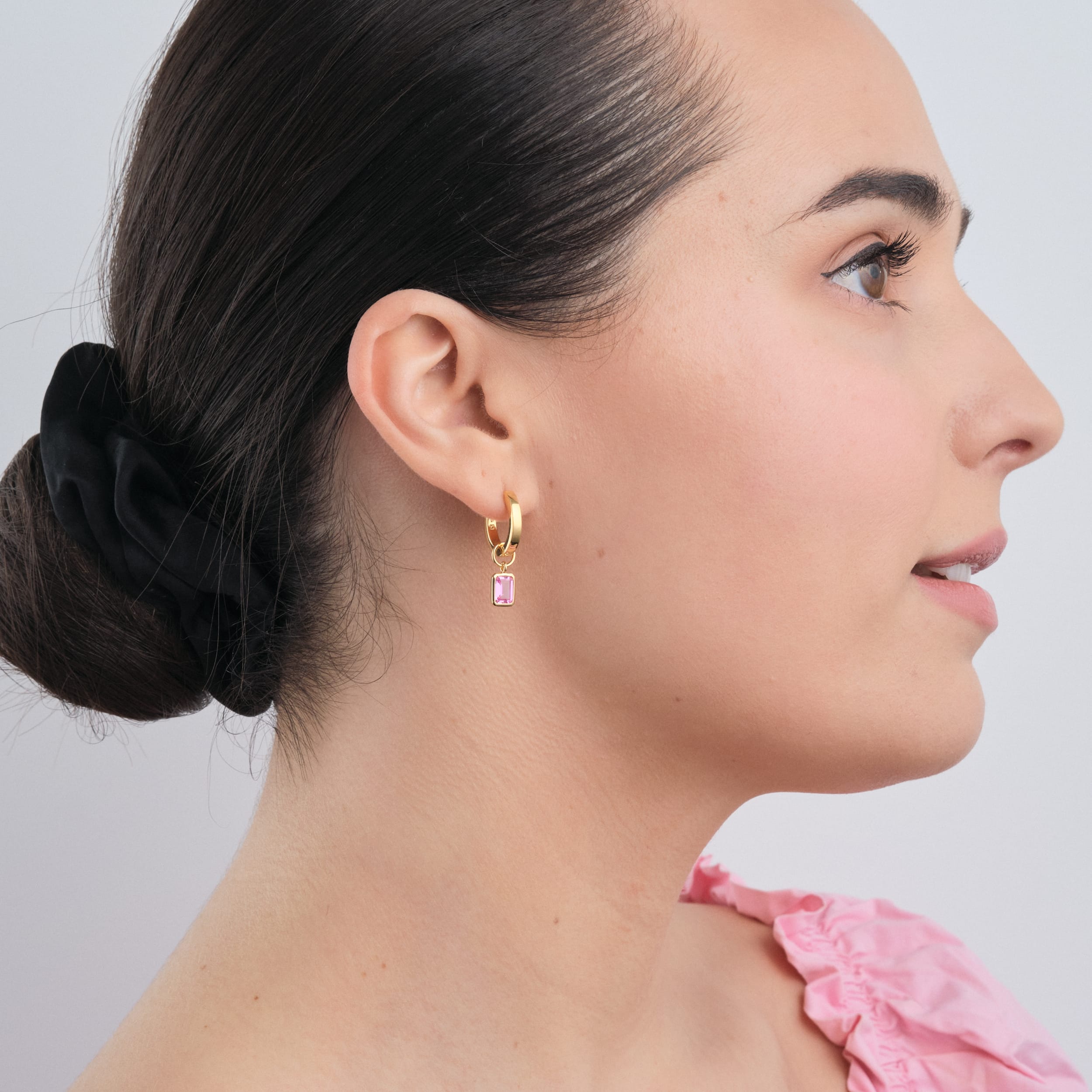 Side view of a woman wearing 18K gold vermeil huggie hoop earrings with interchangeable pink ruby gemstone charms. A stylish, durable, and affordable luxury accessory that can be customised for any occasion.