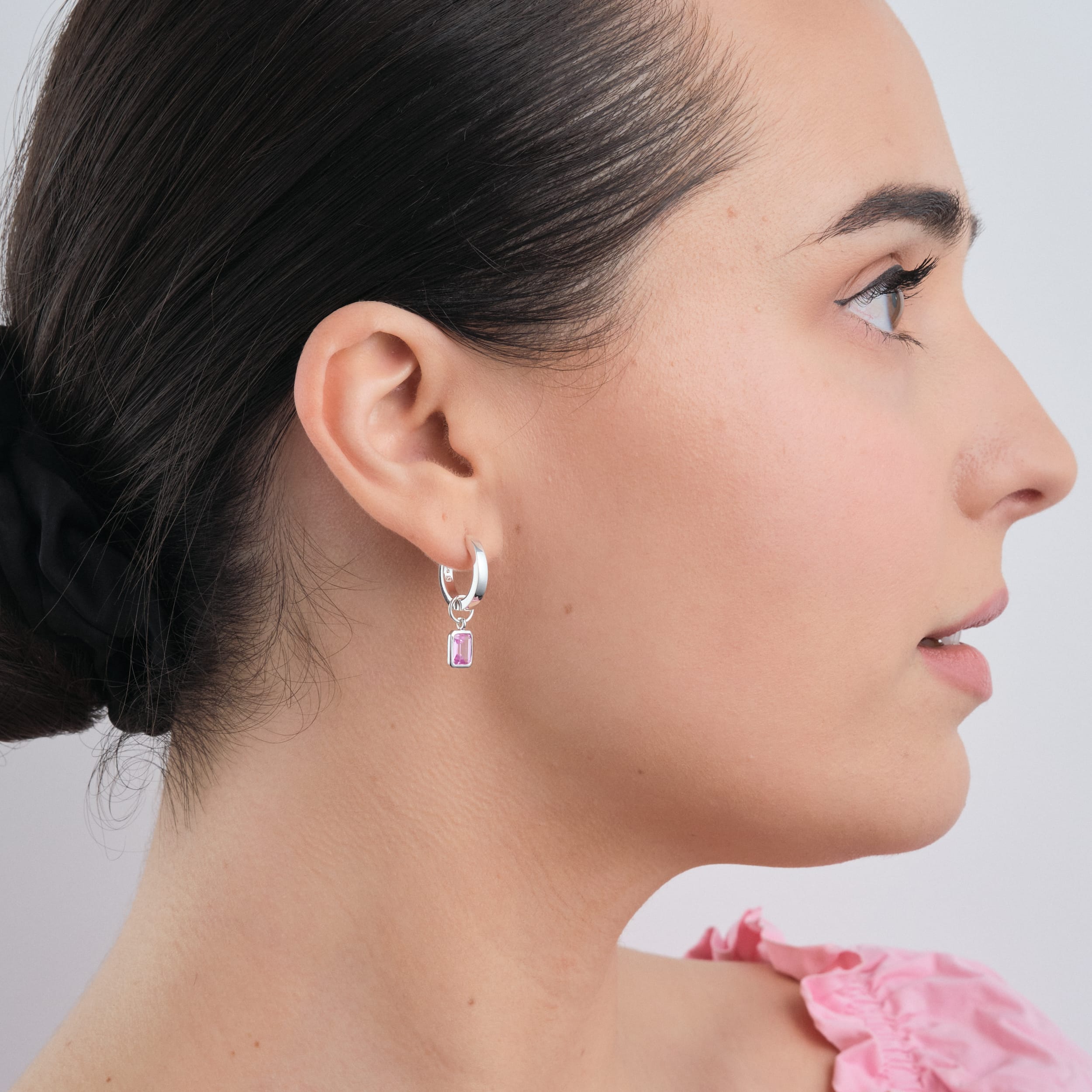 Side view of a woman wearing tarnish free sterling silver huggie hoop earring made from quality materials with a detachable pink ruby gemstone charm.