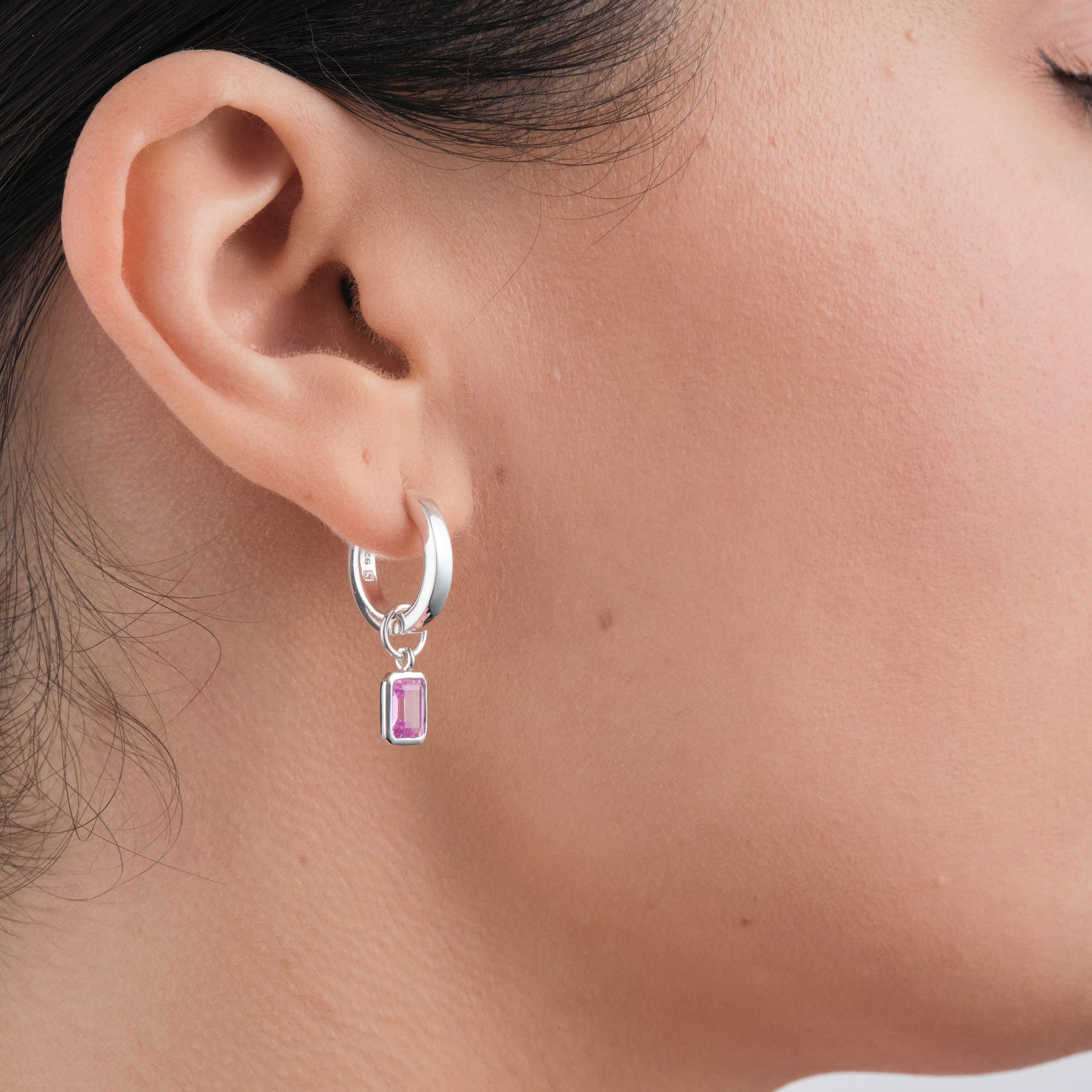 A woman wearing 18K gold vermeil huggie hoop earrings with interchangeable pink ruby gemstone charms a stylish, durable, and affordable luxury accessory that can be customised for any occasion.