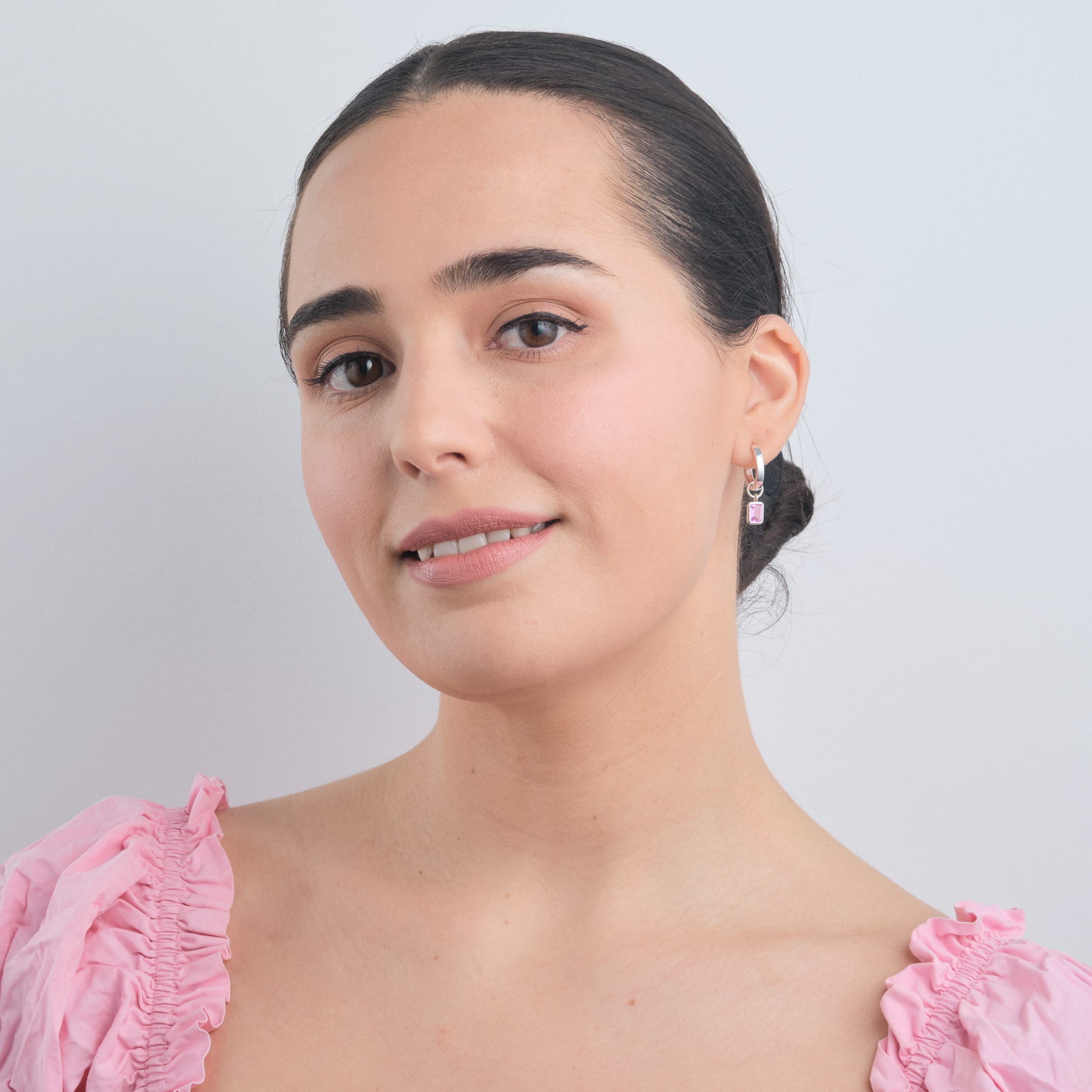 A woman wearing sterling silver huggie hoop earrings with interchangeable pink ruby gemstone charms. Designed with durable, hypoallergenic sterling silver, these earrings are the perfect customisable accessory for any occasion.