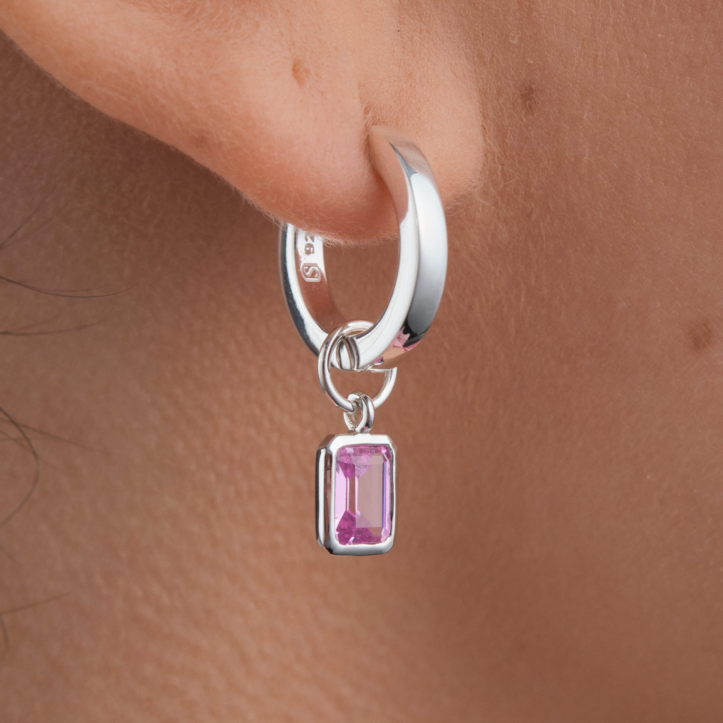 Close-up of sterling silver huggie hoop earrings with interchangeable pink ruby gemstone charms. Showcasing the versatility of sterling silver with a vibrant pink ruby charm. A perfect addition to any jewellery collection for everyday wear or special occasions.