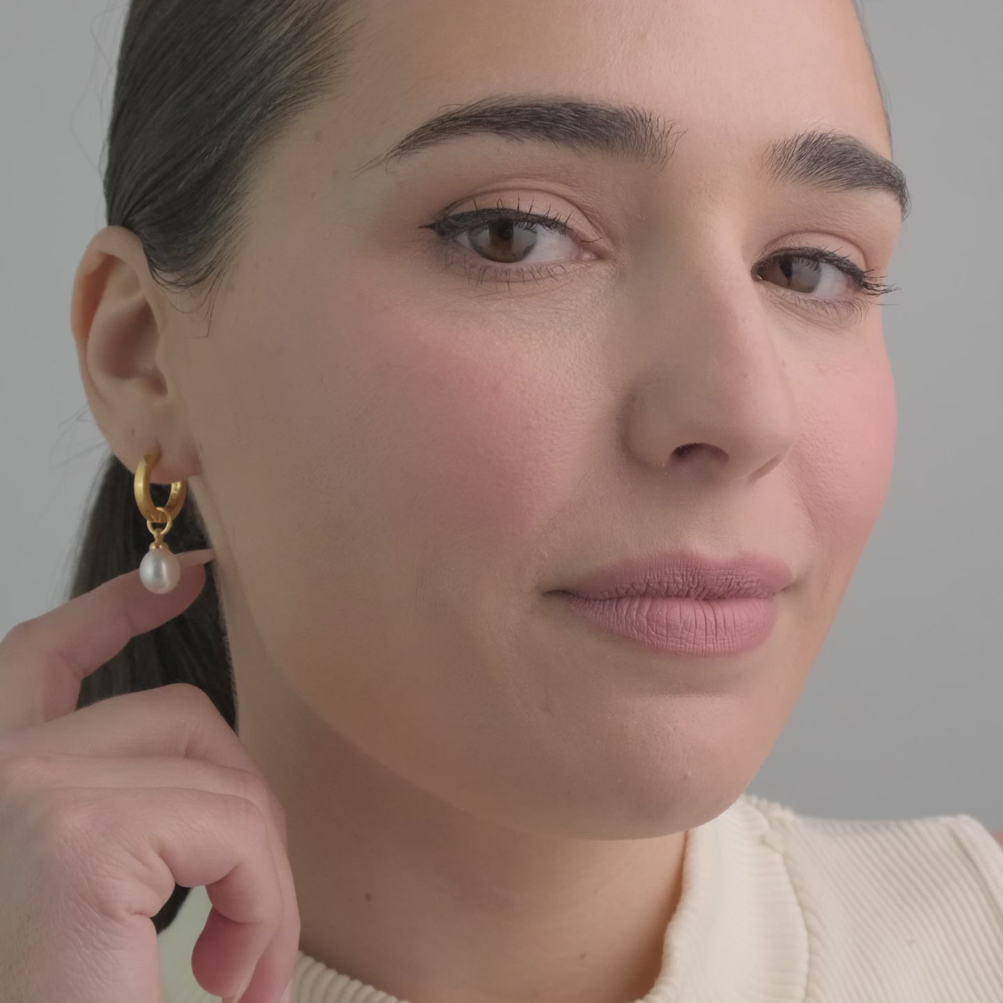 Video of a woman wearing 18K gold vermeil huggie hoop earrings with interchangeable pearl charms. The perfect addition to wedding jewellery, offering versatility and style. Crafted from durable 18K gold vermeil, these earrings are an affordable luxury choice for a meaningful gift.