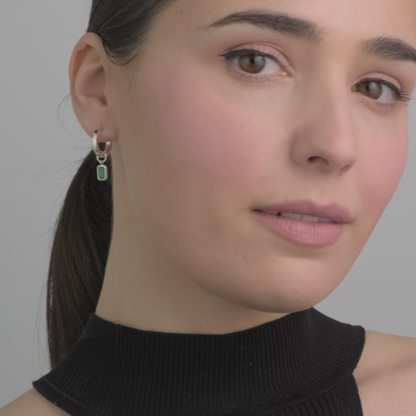Video of a woman wearing Sterling silver huggie hoop earrings with interchangeable green onyx gemstone charms featuring the rich green onyx, the birthstone for May, set in hypoallergenic sterling silver. A customisable and elegant choice, perfect for everyday wear or as a meaningful gift.