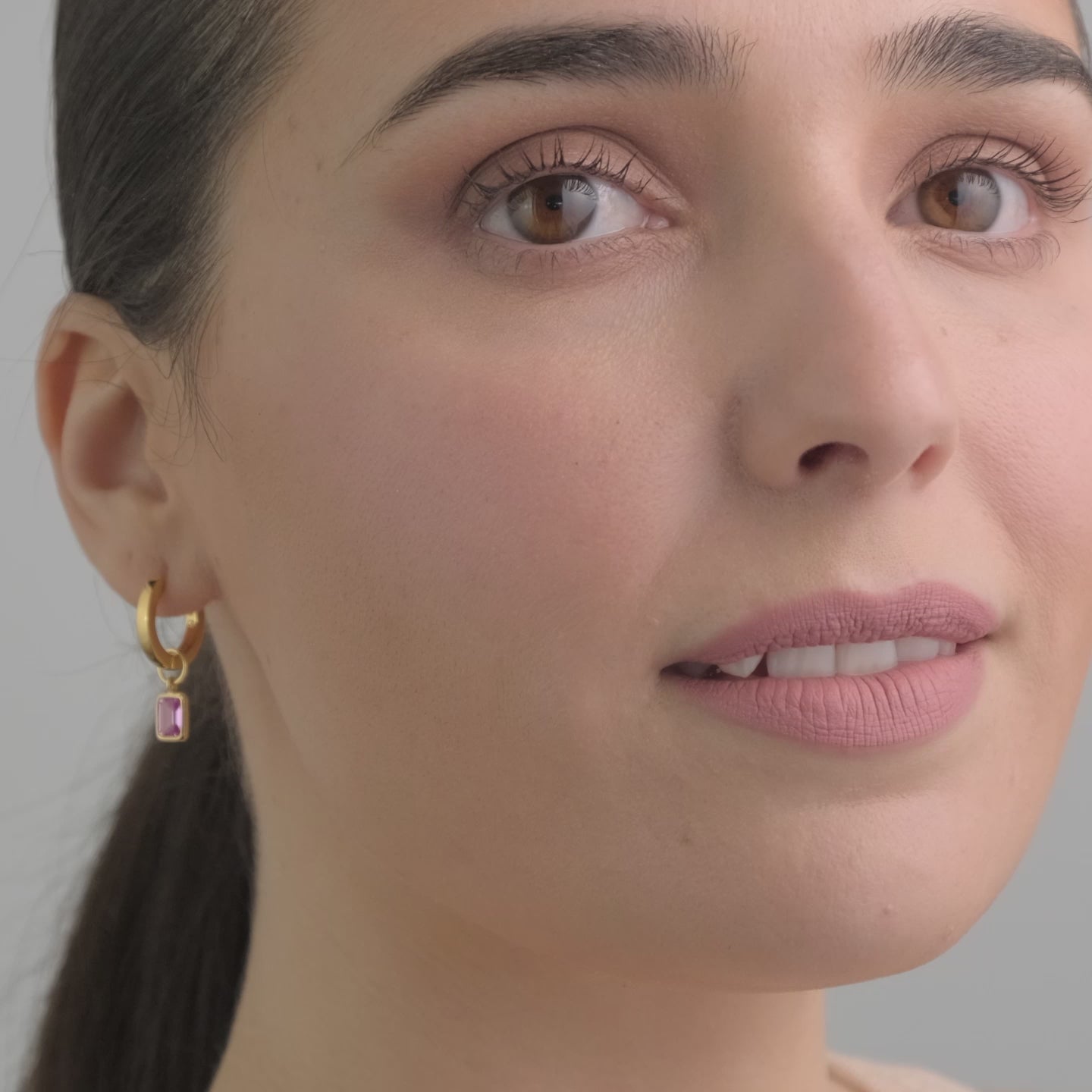 Video of a woman wearing 18k gold vermeil huggie hoop earrings with detachable pink ruby gemstone charms. The perfect pop of colour for any outfit.