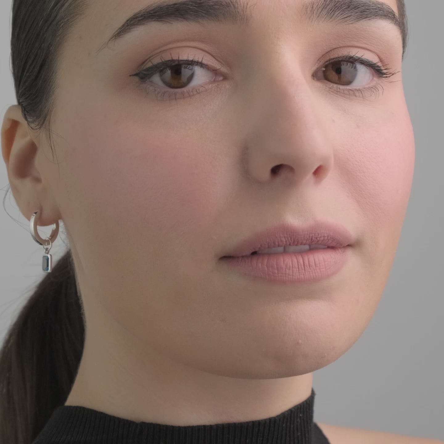 Video of a beautiful woman wearing sterling silver huggie hoop earring with blue topaz charms.