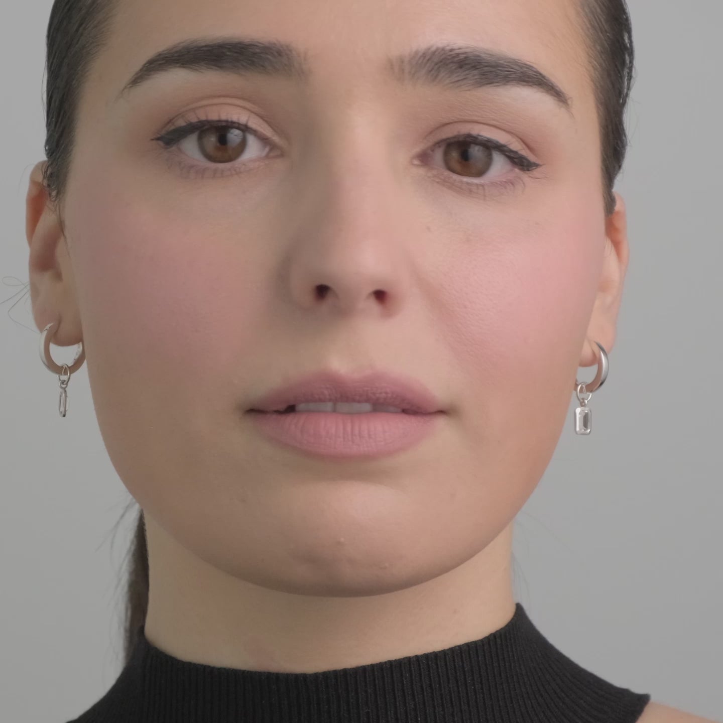 A video of a woman wearing sterling silver huggie hoop earrings with interchangeable white topaz charms.