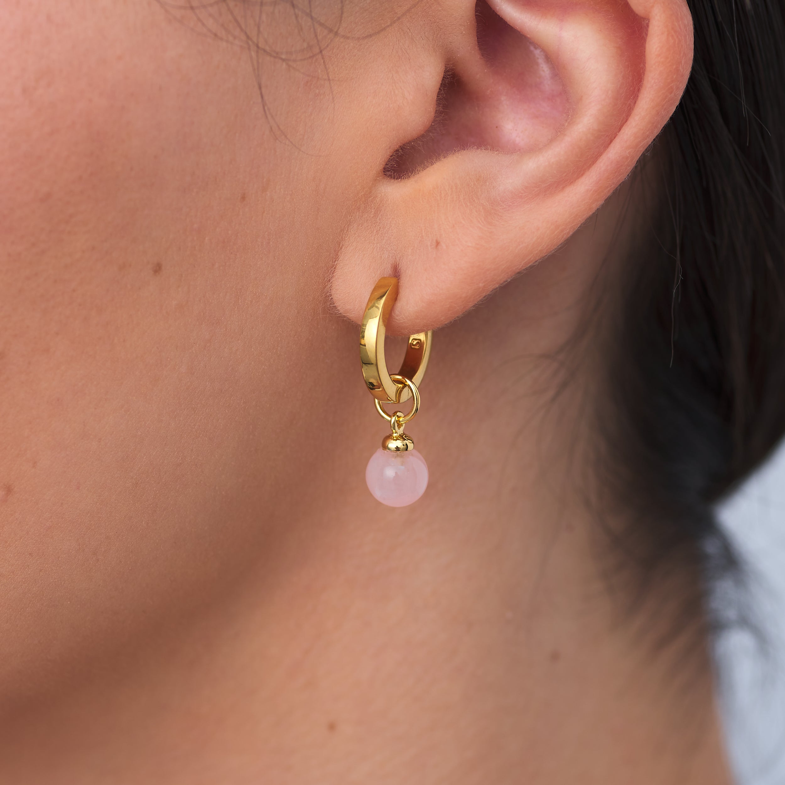 Minimalist 18k Gold Vermeil Huggie hoop earrings with customisable Rose Quartz gemstone charm attached to woman's earlobe.