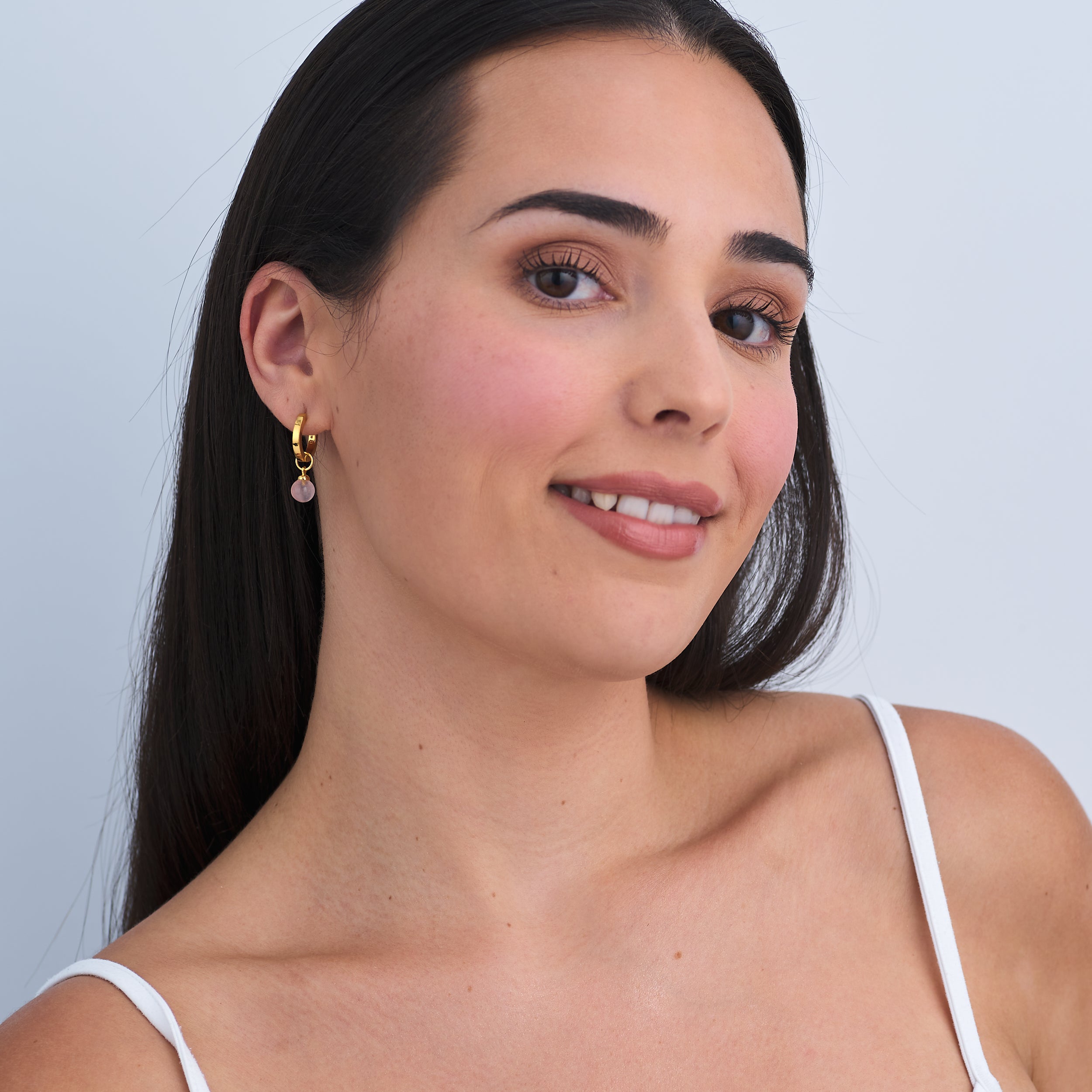 Every day wear 18k Gold Vermeil Huggie hoop earrings with customisable Rose Quartz gemstone charm attached worn by a beautiful woman.