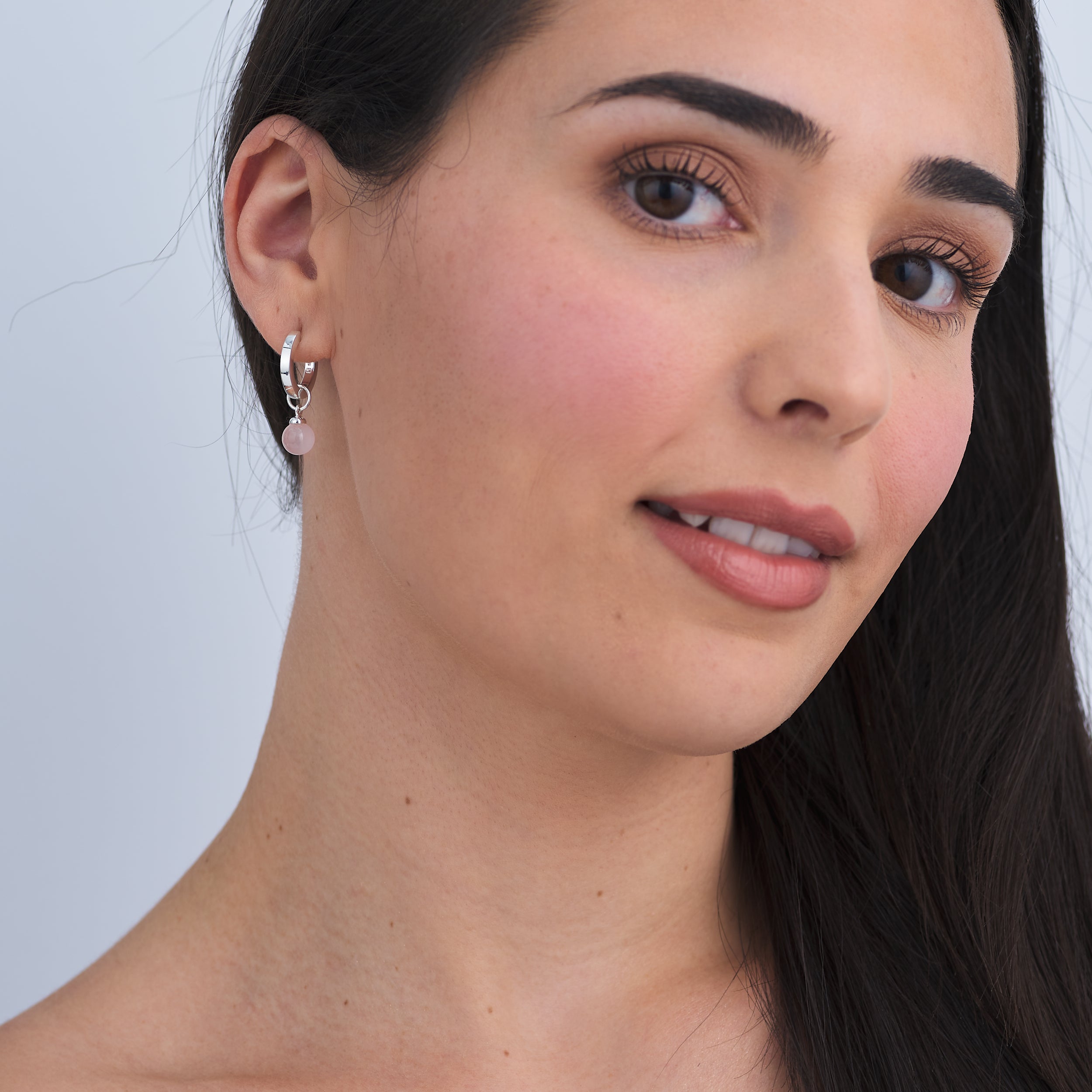 Woman wearing high-end Sterling Silver Huggie hoop earrings with interchangeable Rose Quartz gemstone charm attached.