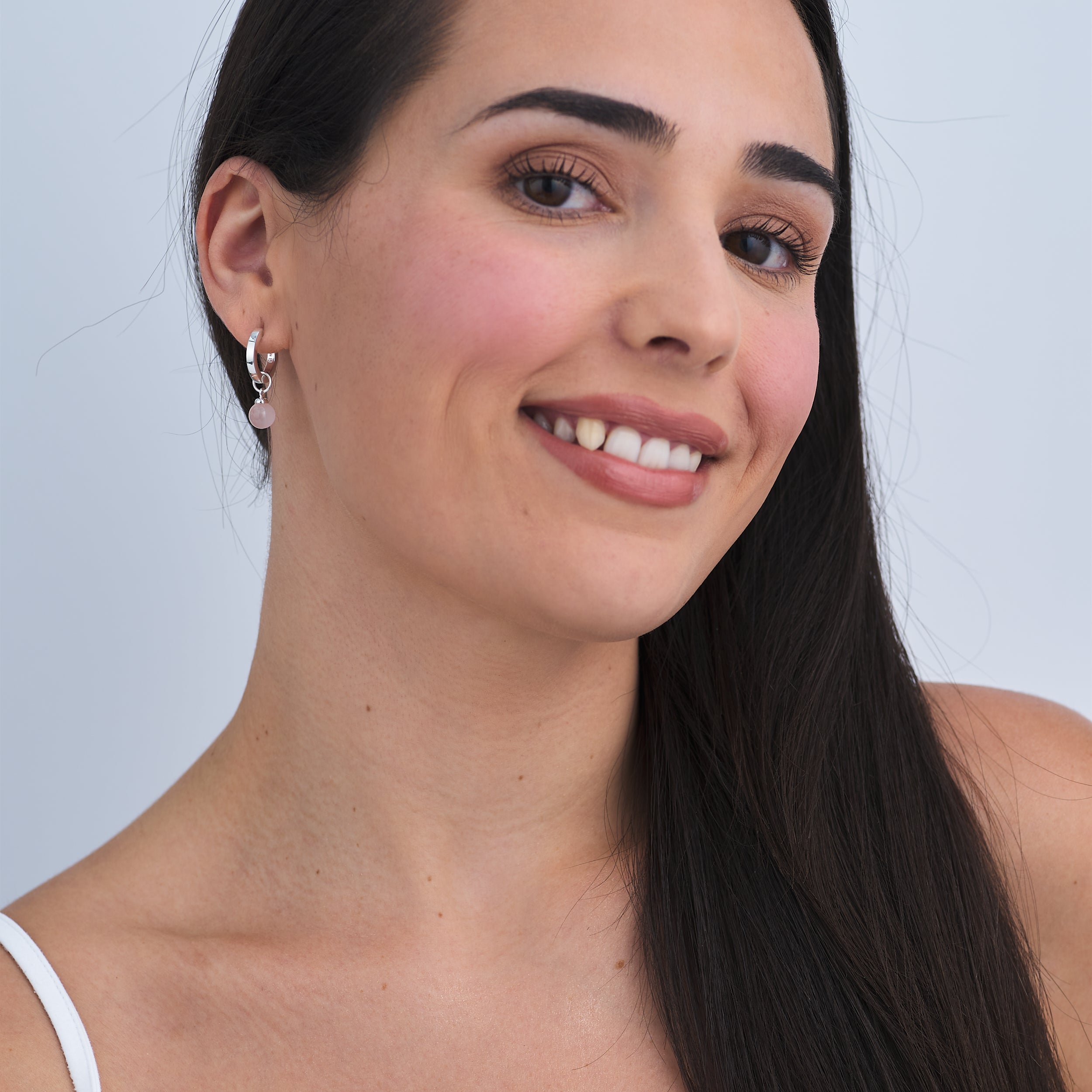 Woman wearing hypoallergenic Sterling Silver Huggie hoop earrings with interchangeable Rose Quartz gemstone charms attached.