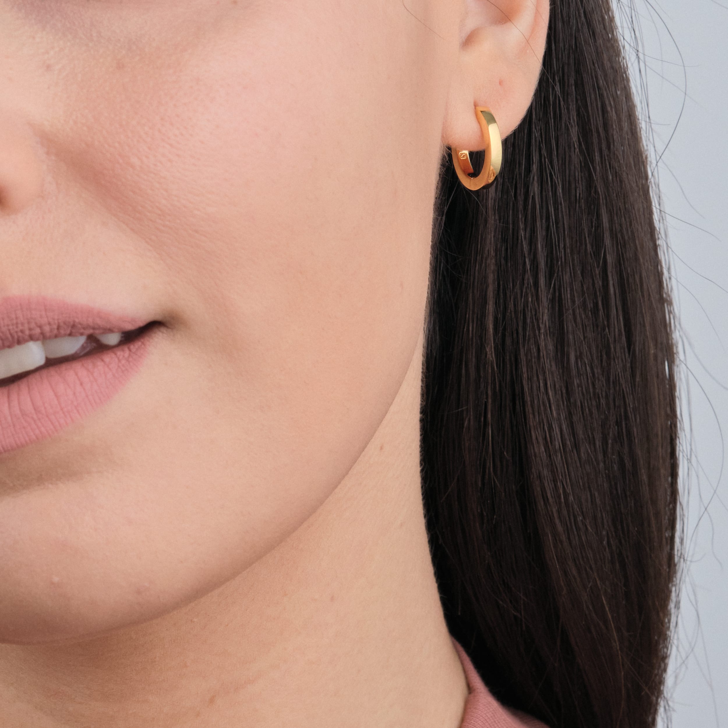 Close-up of 18K gold vermeil huggie hoops. Durable, cost-effective, and nickel-free, offering a high-end look without the price tag.