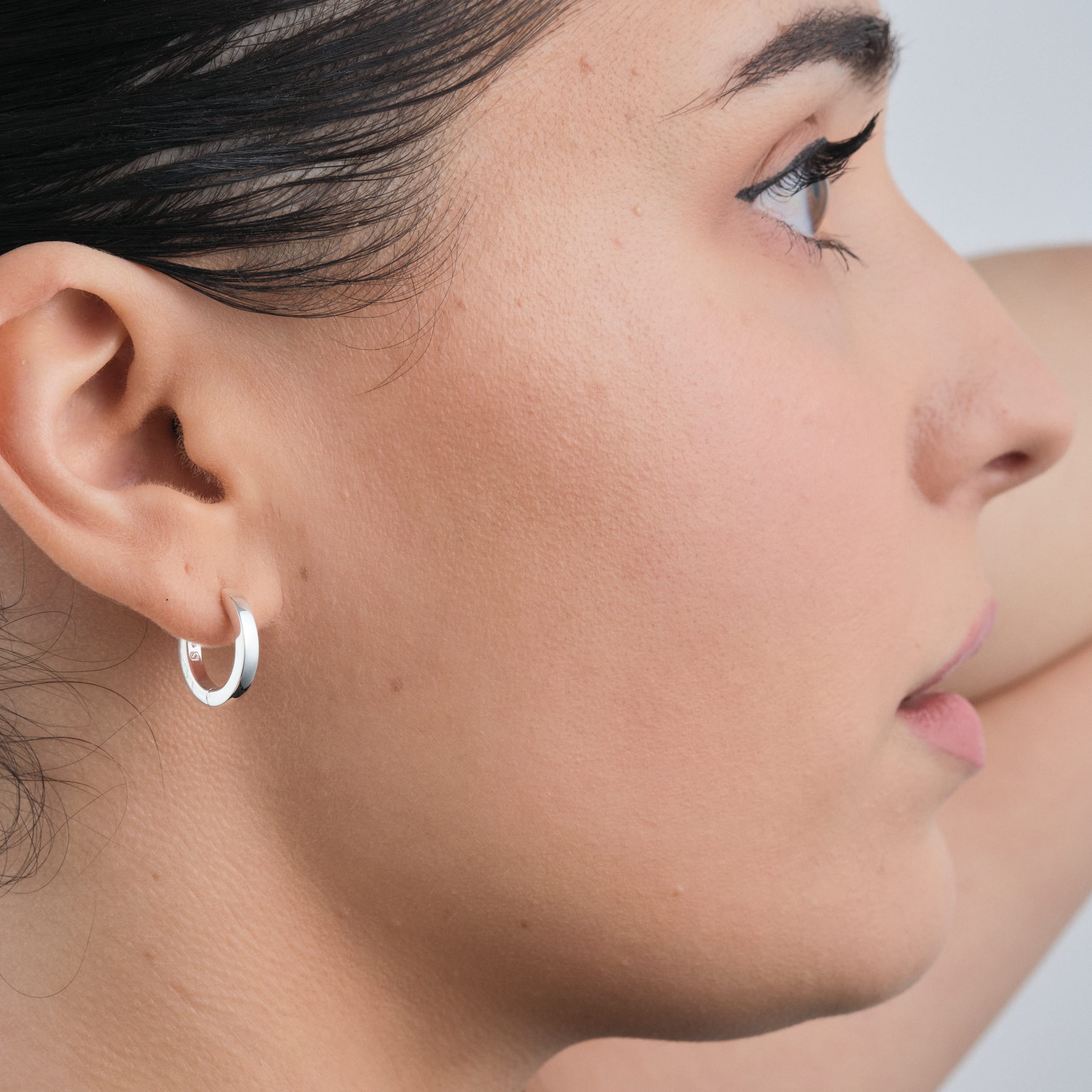 Close-up of sterling silver huggie hoop earrings. A timeless, cost-effective, and hypoallergenic choice for effortless style and comfort.
