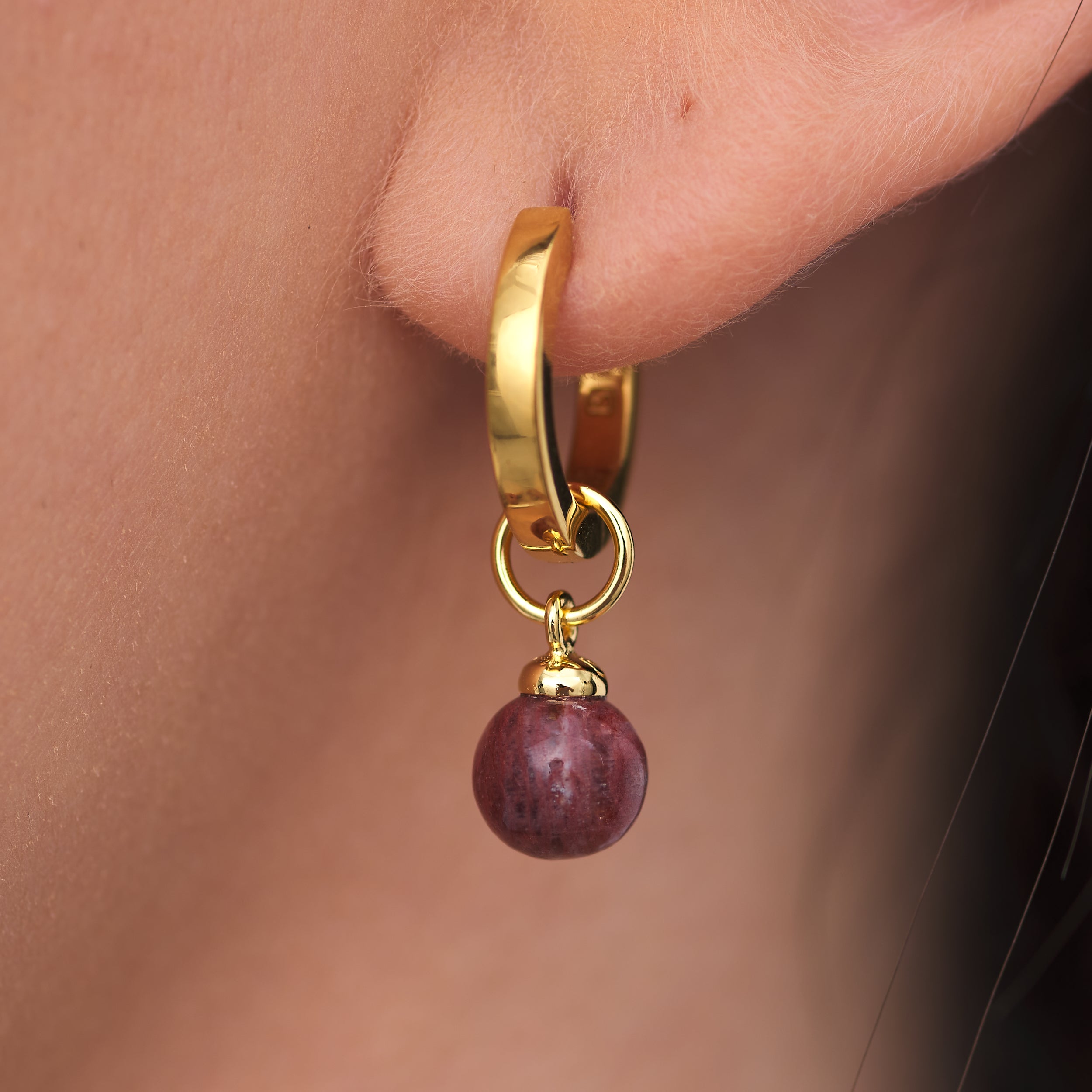 Close up of 18k Gold Vermeil Huggie hoop earring with interchangeable Sunstone Jasper gemstone charm attached to woman's earlobe.