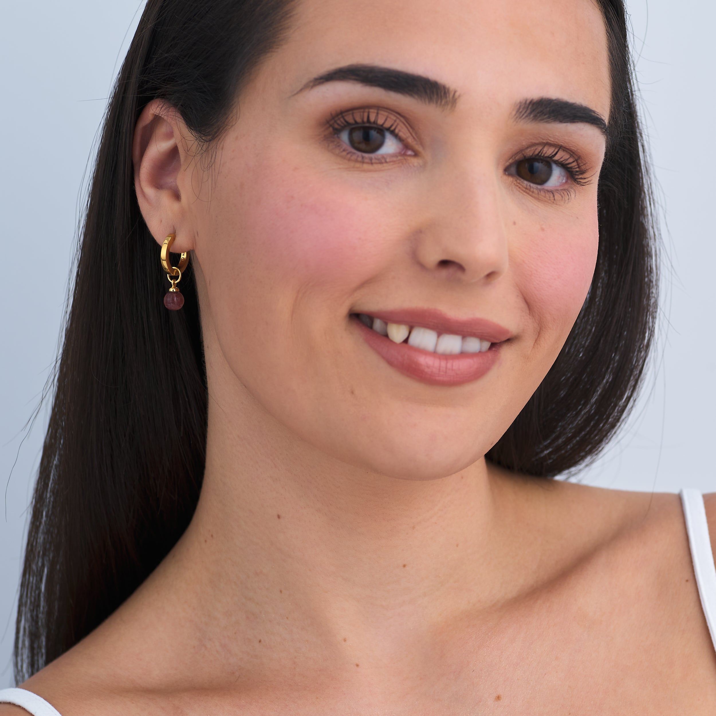 Beautiful woman wearing timeless 18k Gold Vermeil Huggie hoop earrings with interchangeable Sunstone Jasper gemstone charm attached.