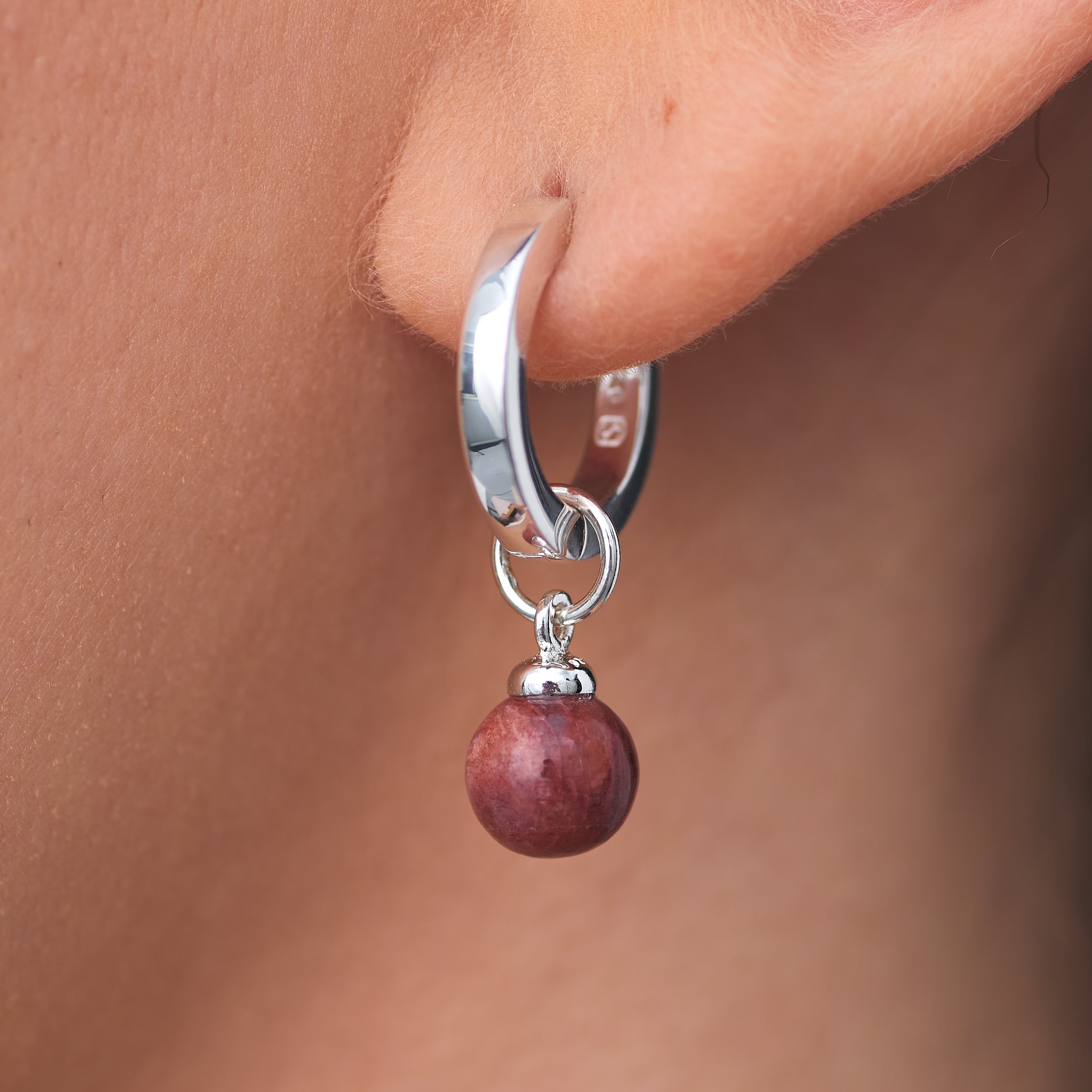 Beautiful Sterling Silver Huggie hoop earring with interchangable Sunstone Jasper gemstone charm attached to a woman's earlobe.