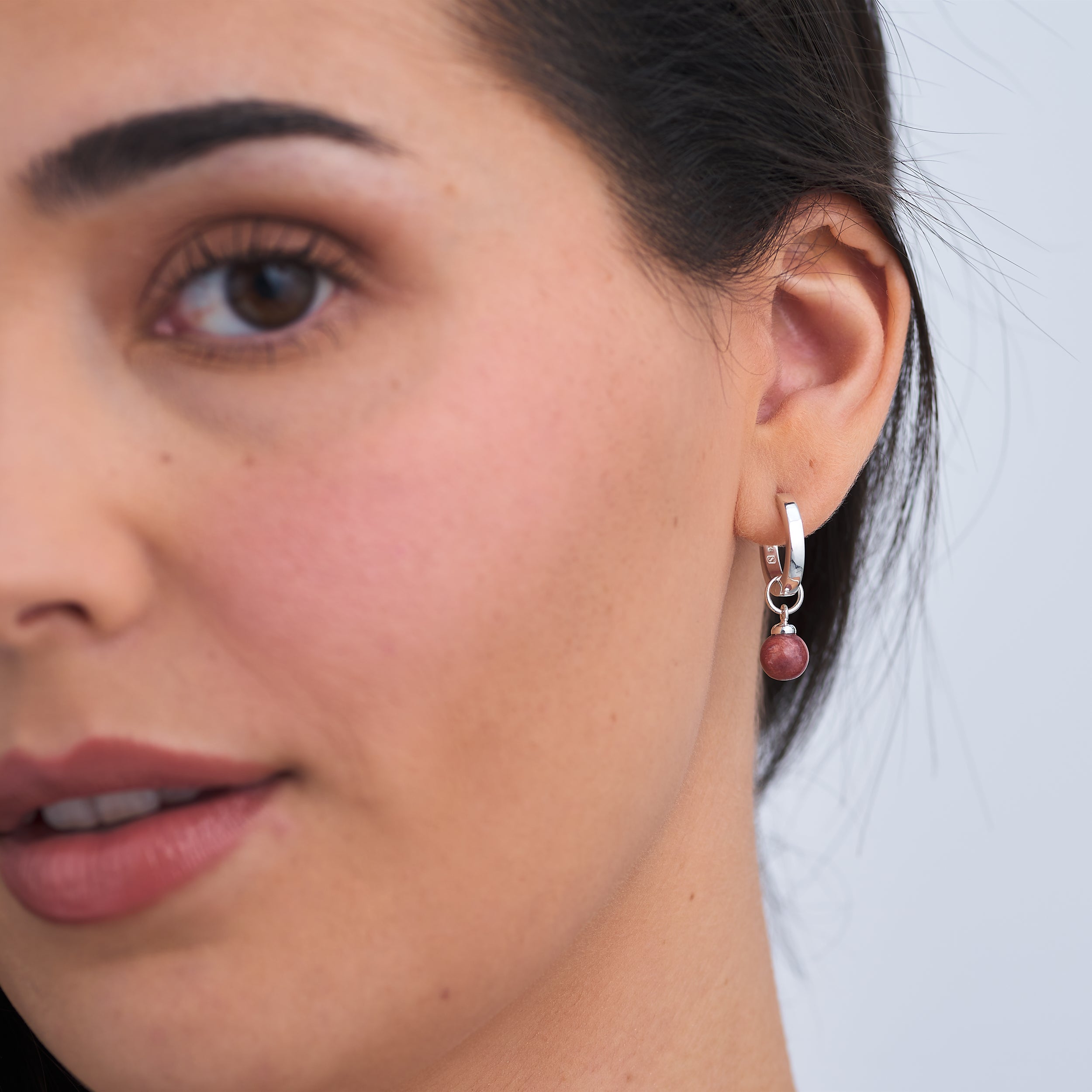 Close up of a beautiful woman wearing Sterling Silver Huggie hoop earrings with interchangeable Sunstone Jasper gemstone charm attached.