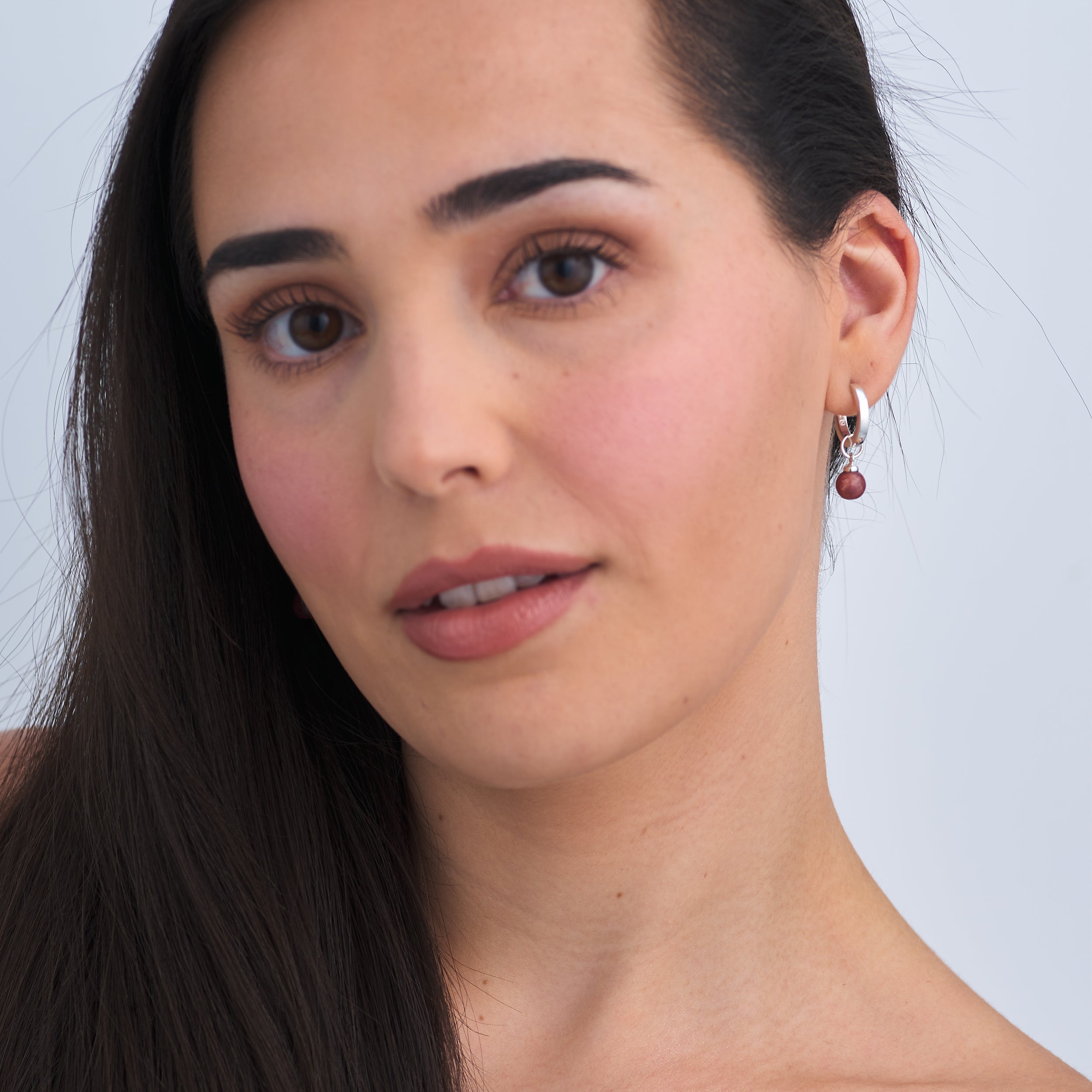 Beautiful woman wearing Sterling Silver Huggie hoop earrings with interchangeable Sunstone Jasper gemstone charm attached.