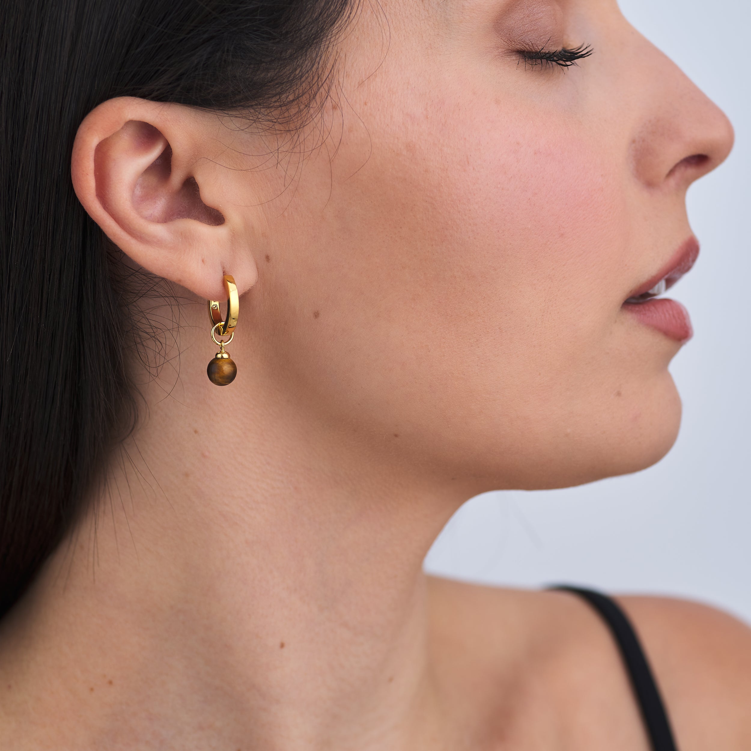 Woman wearing everyday wear 18k Gold Vermeil Huggie Hoop earrings with customisable Tiger's eye gemstone charms.