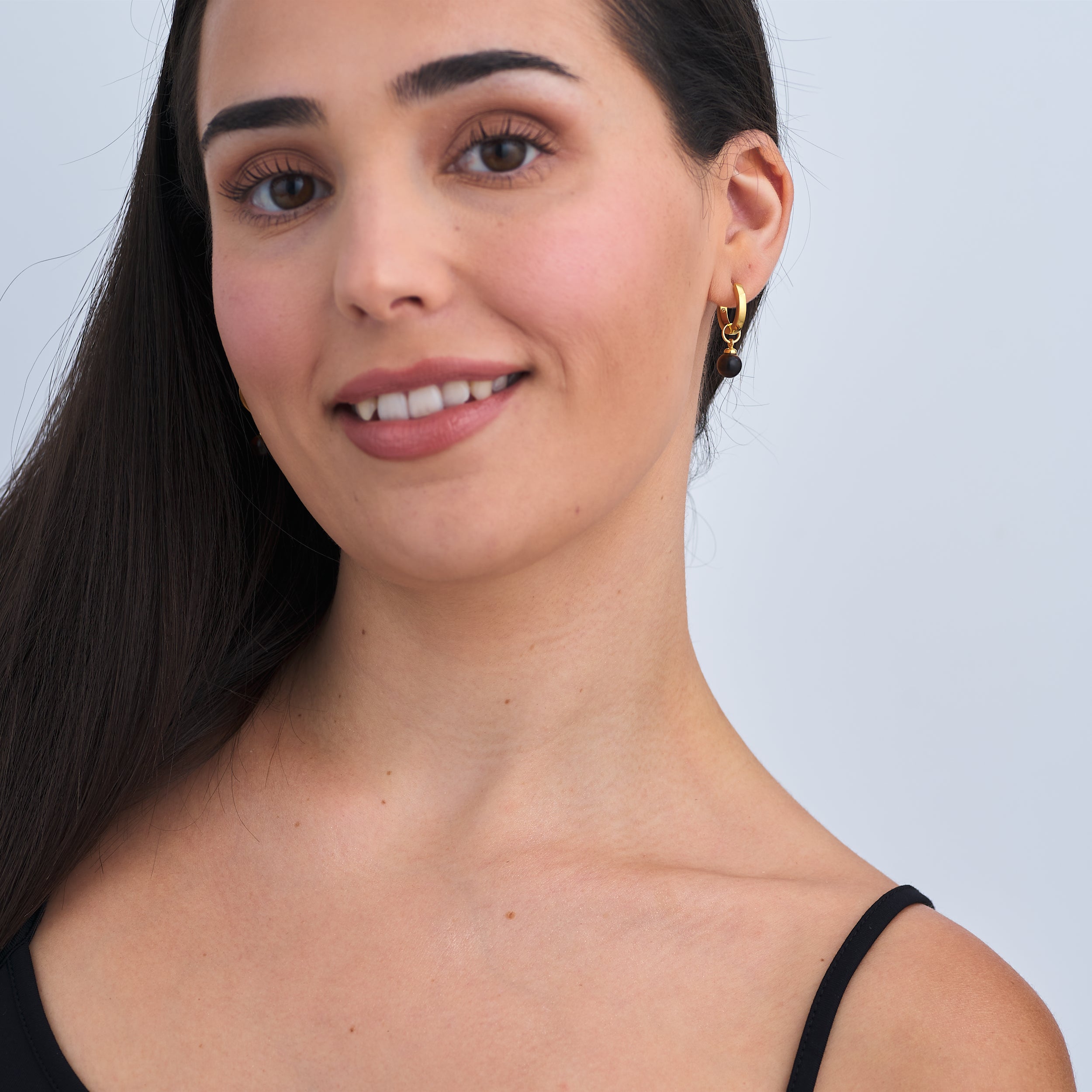 Elegant woman wearing 18k Gold Vermeil Huggie Hoop earrings with interchangeable Tiger's eye gemstone charm attached.
