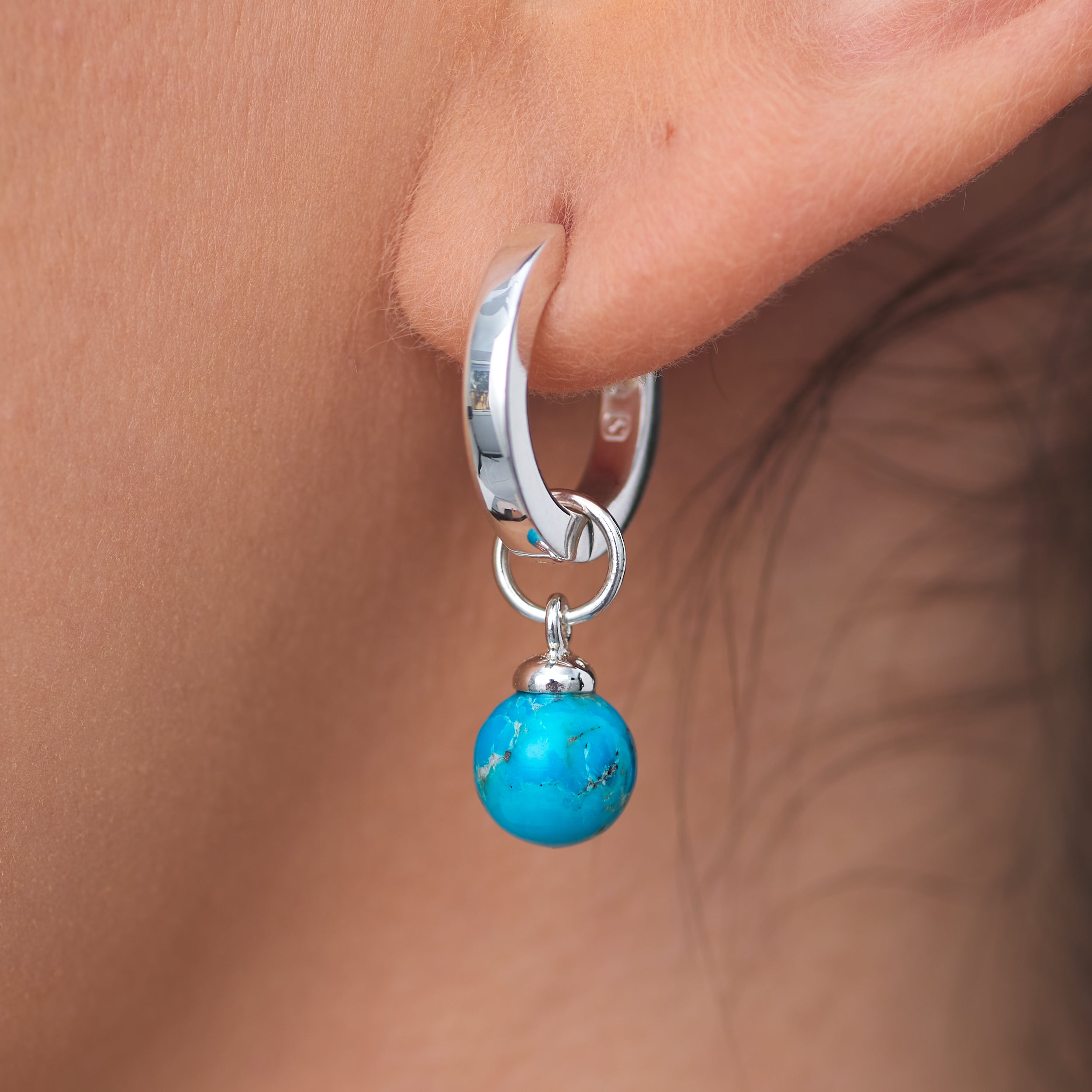 High quality Sterling Silver Huggie hoop earrings with interchangeable Turquoise charms attached to a woman's ear lobe.