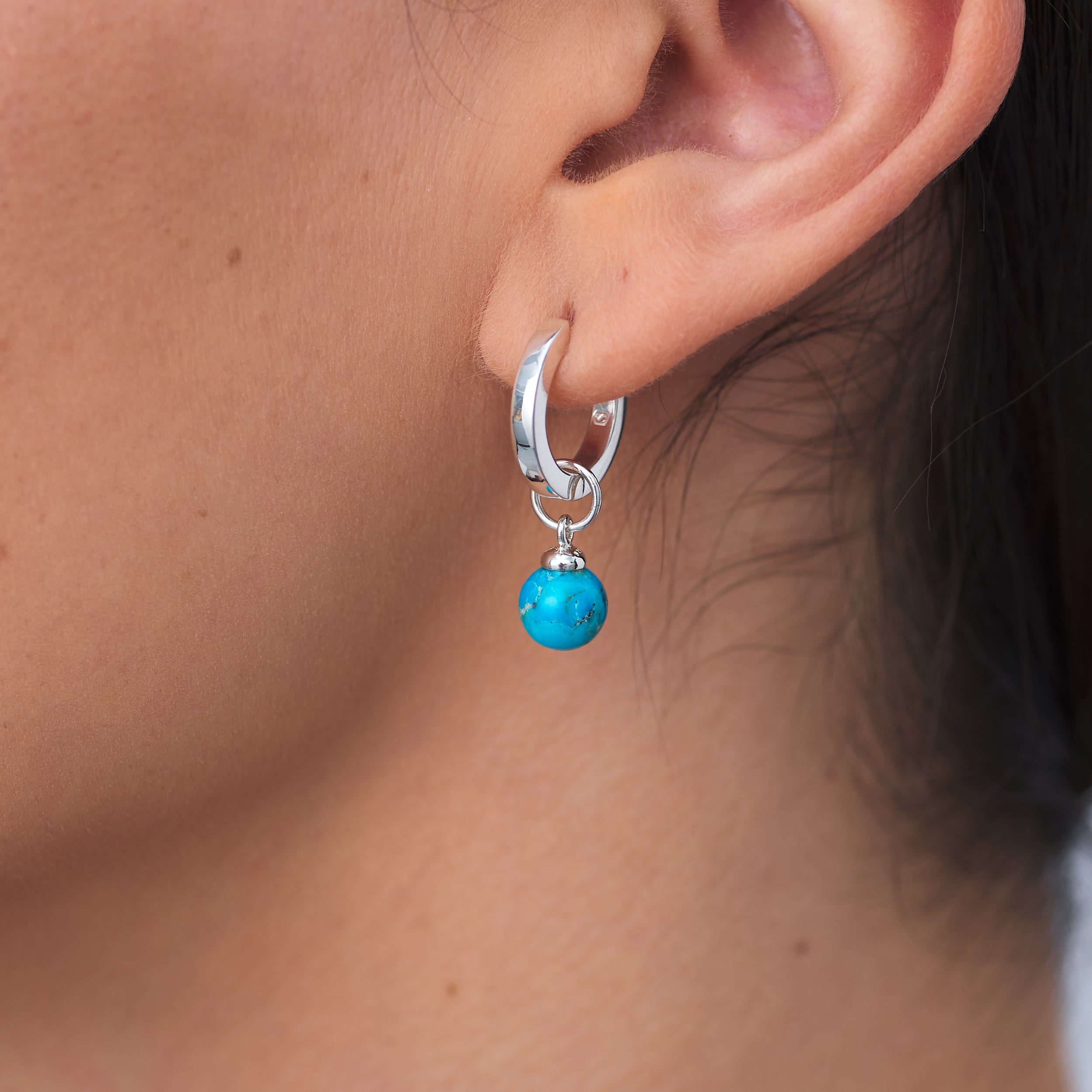 Close up of modern elegant Sterling Silver Huggie Hoop earrings with a customisable Turquoise charm attached to a woman's ear.