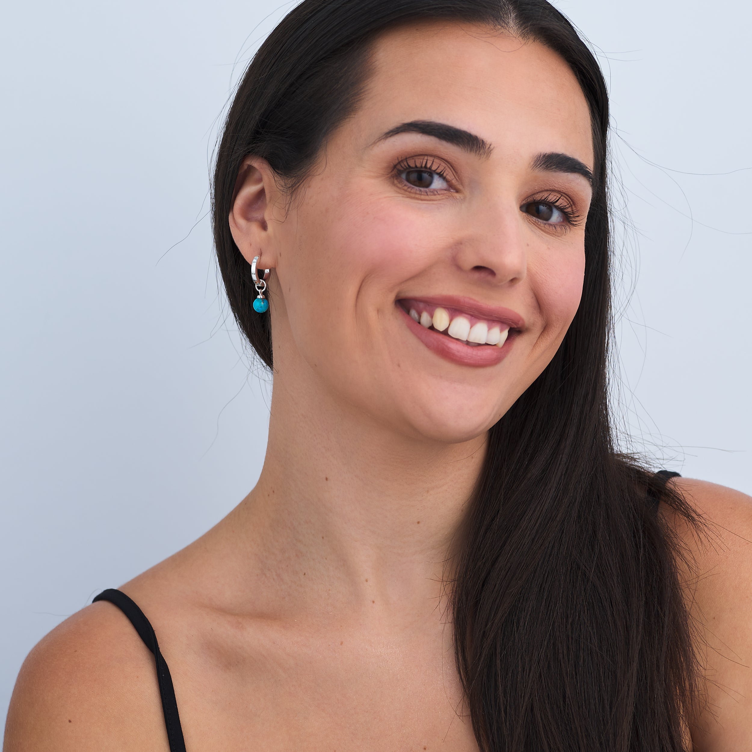 Fine handcrafted Sterling Silver Huggie Hoop earrings with detachable Turquoise charm attached worn by a beautiful woman.
