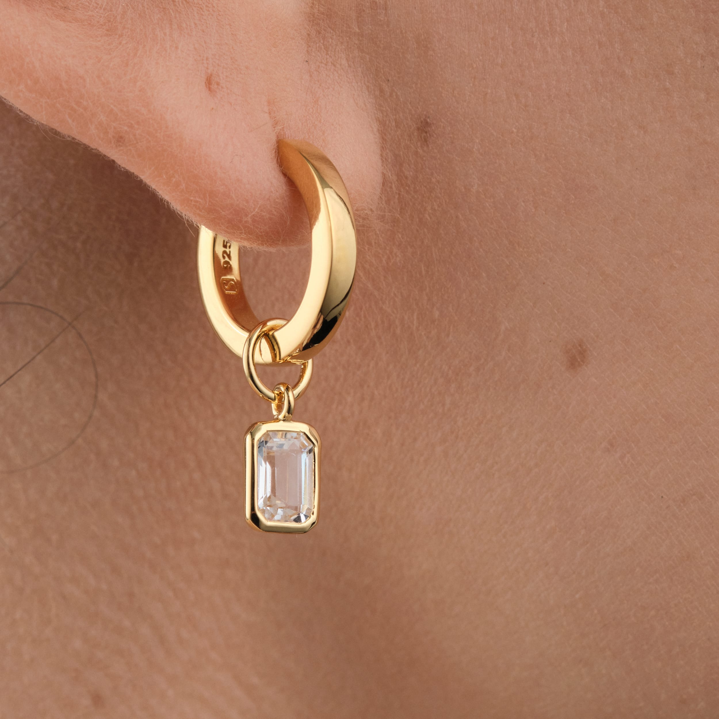 Close up of a white topaz gemstone interchangeable charm to durable 18k gold vermeil huggie hoop earrings. Perfect for chic sophisticated looks.