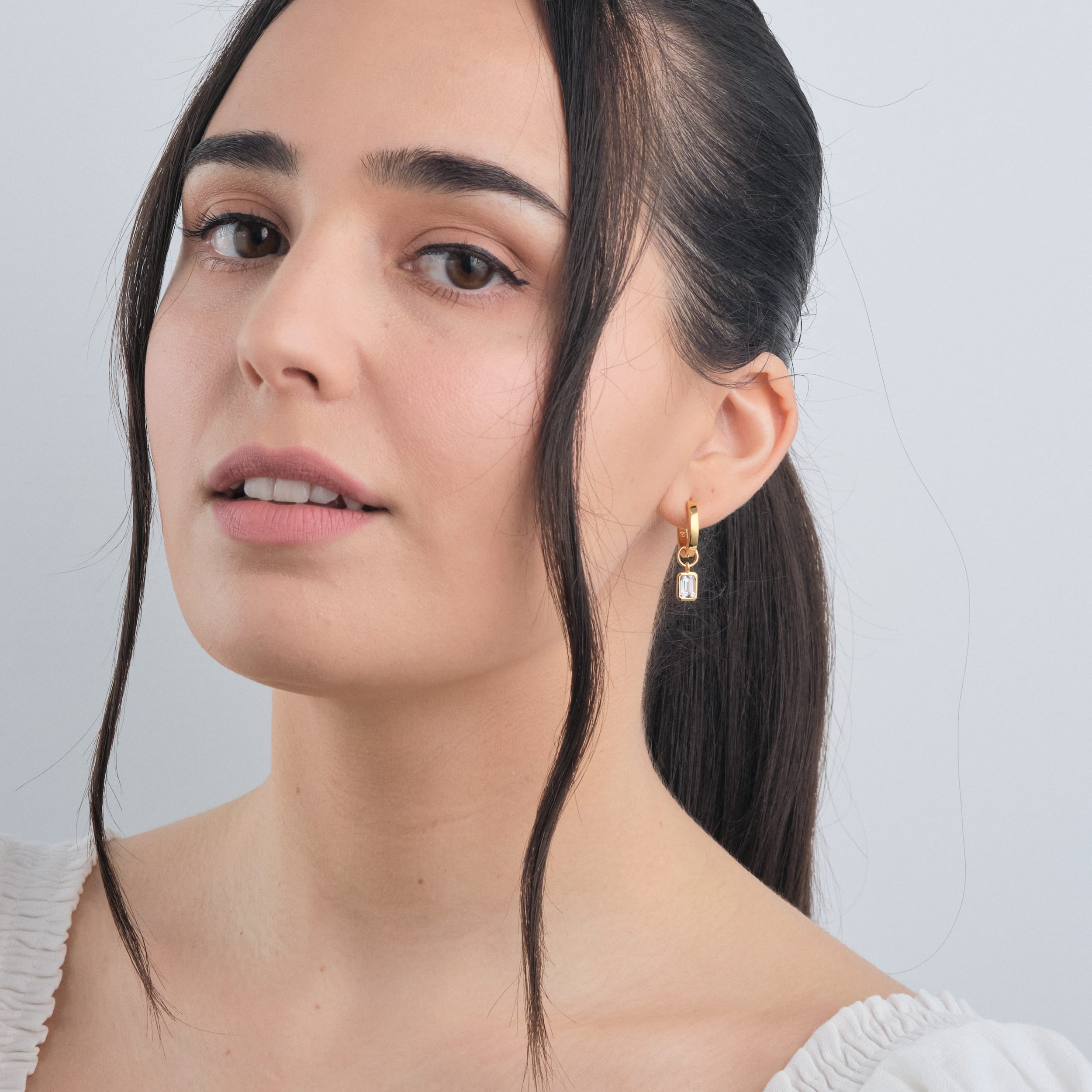 Woman wearing 18K gold vermeil huggie hoop earrings with interchangeable white topaz gemstone charms made with high-quality, long-lasting gold vermeil, these earrings offer a sophisticated and budget-friendly way to elevate any look.