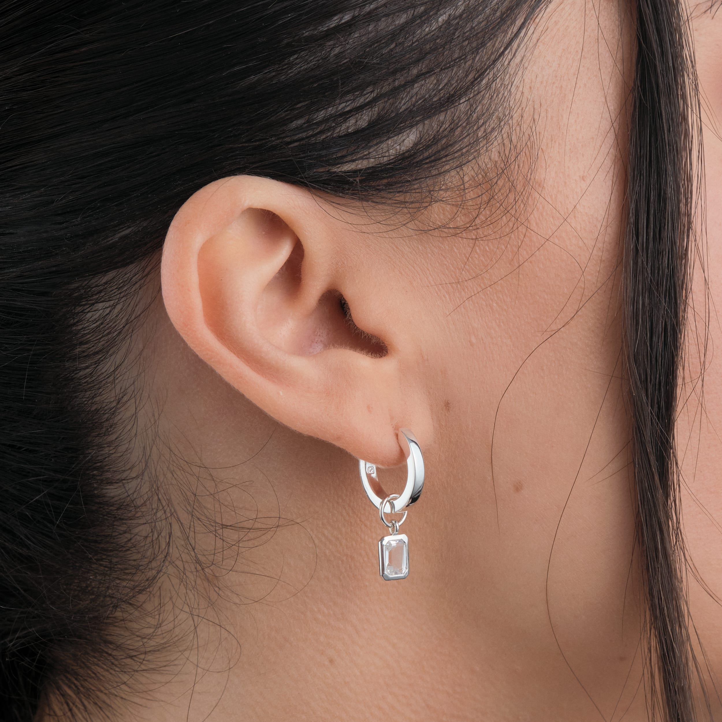 Close up of nickel free sterling silver huggie hoop earrings worn by a woman with detachable white topaz gemstone charms.