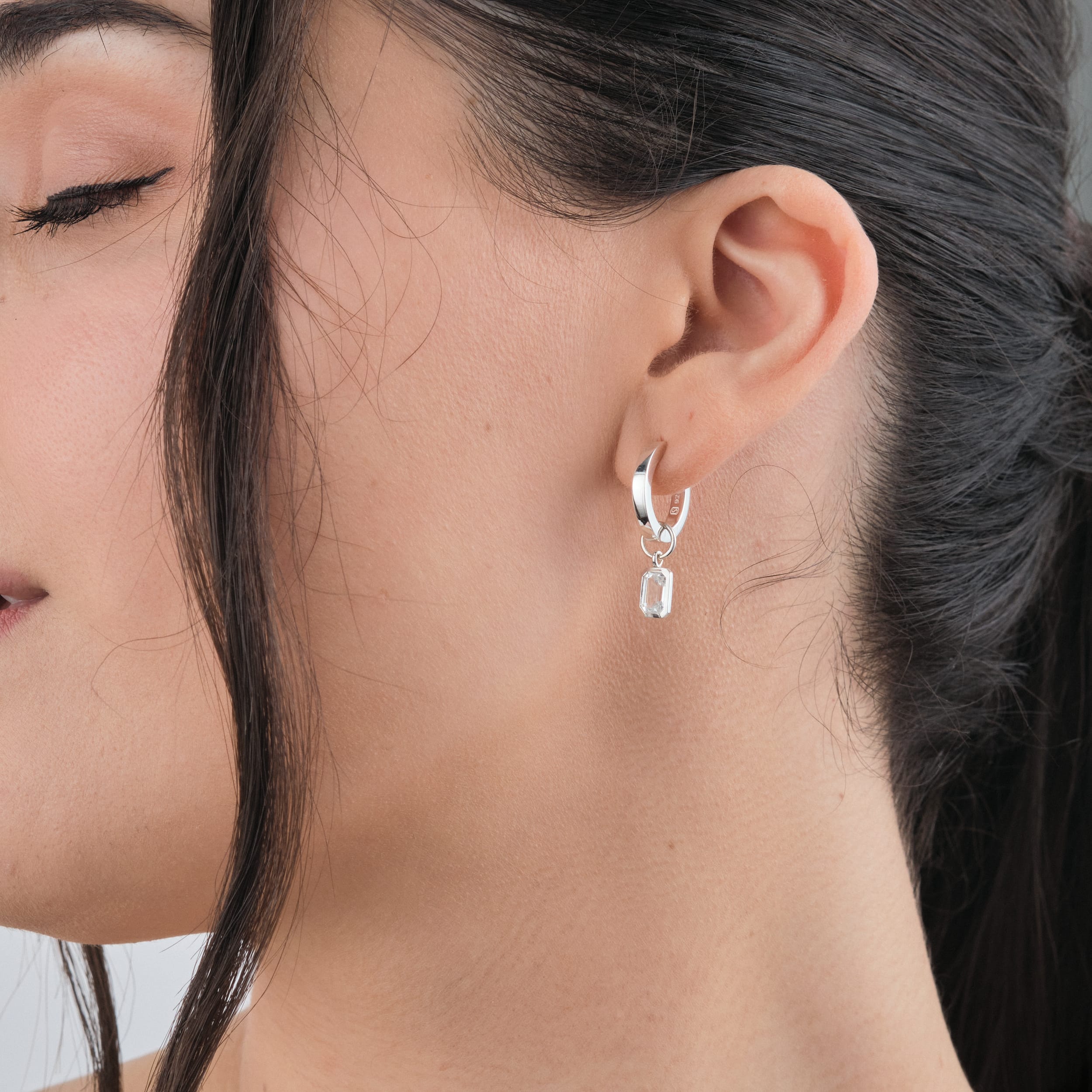 Side view of a woman wearing beautiful white topaz gemstone charm earrings with durable and tarnish free huggie hoop earrings. Perfect for sensitive skin and those who love customisable designs.
